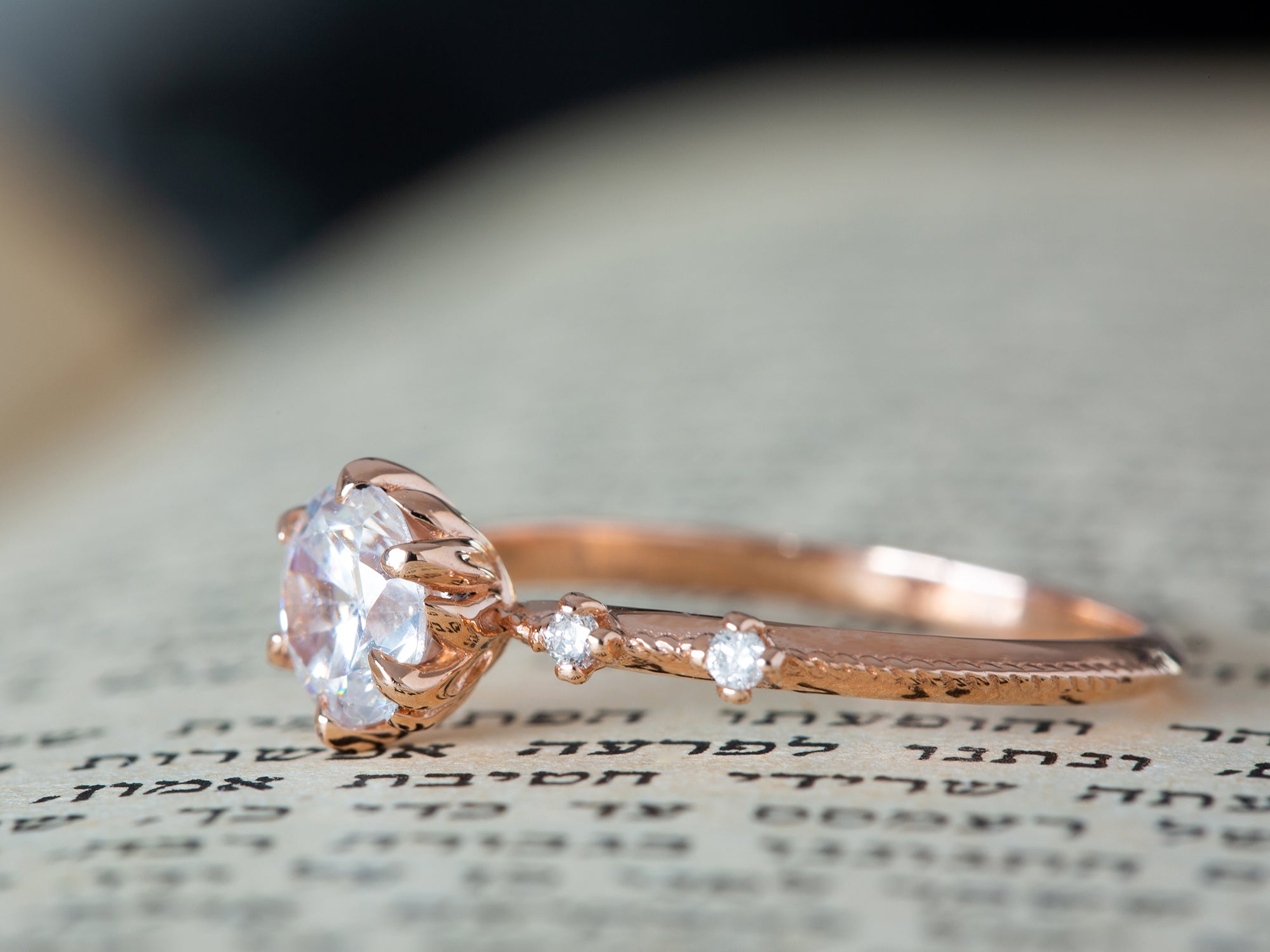 טבעת יהלום פרח בזהב אדום משובצת יהלום על רקע של ספר