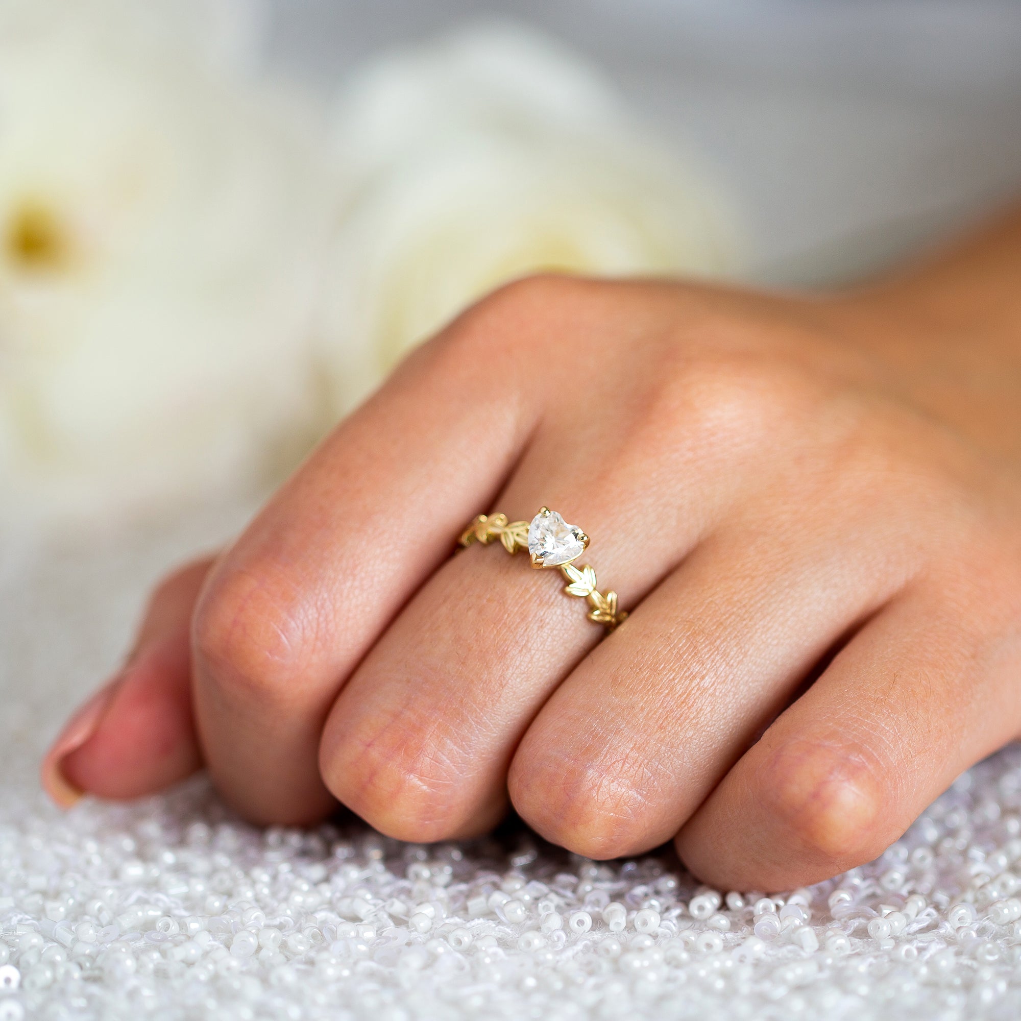 יד של אישה שעונדת טבעת זהב צהוב 14 קראט בעיצוב עלים מיוחד, מושבצת יהלום מרכזי בצורת לב