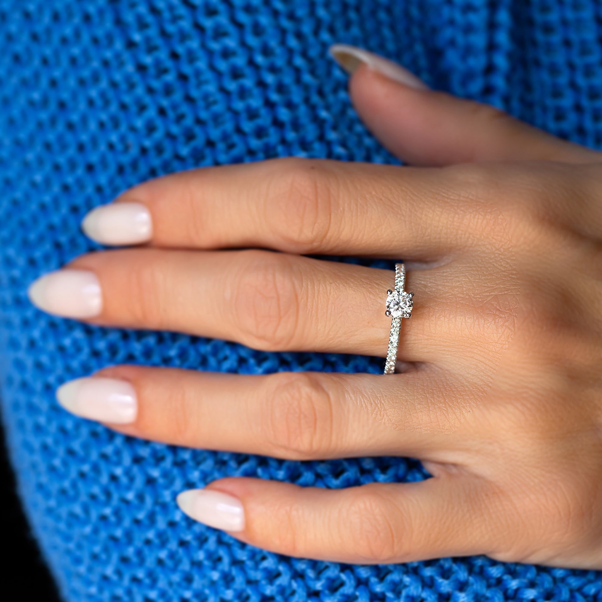 אישה עונדת טבעת סוליטר זהב לבן עדינה על רקע כחול