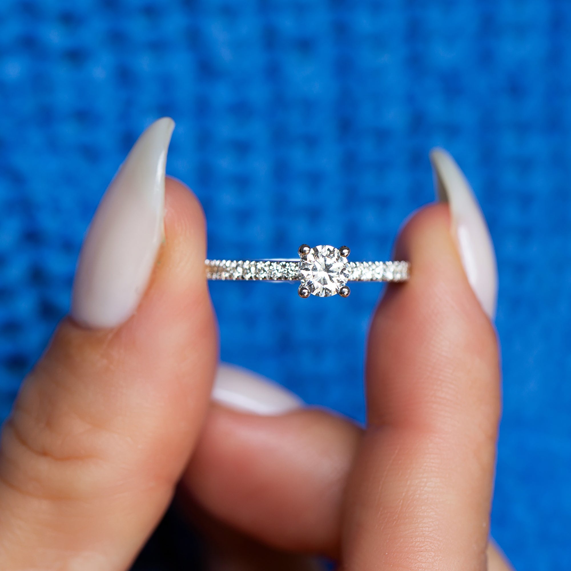 אצבעות של אישה מחזיקות טבעת יהלום עדינה משובצת יהלומים טבעיים