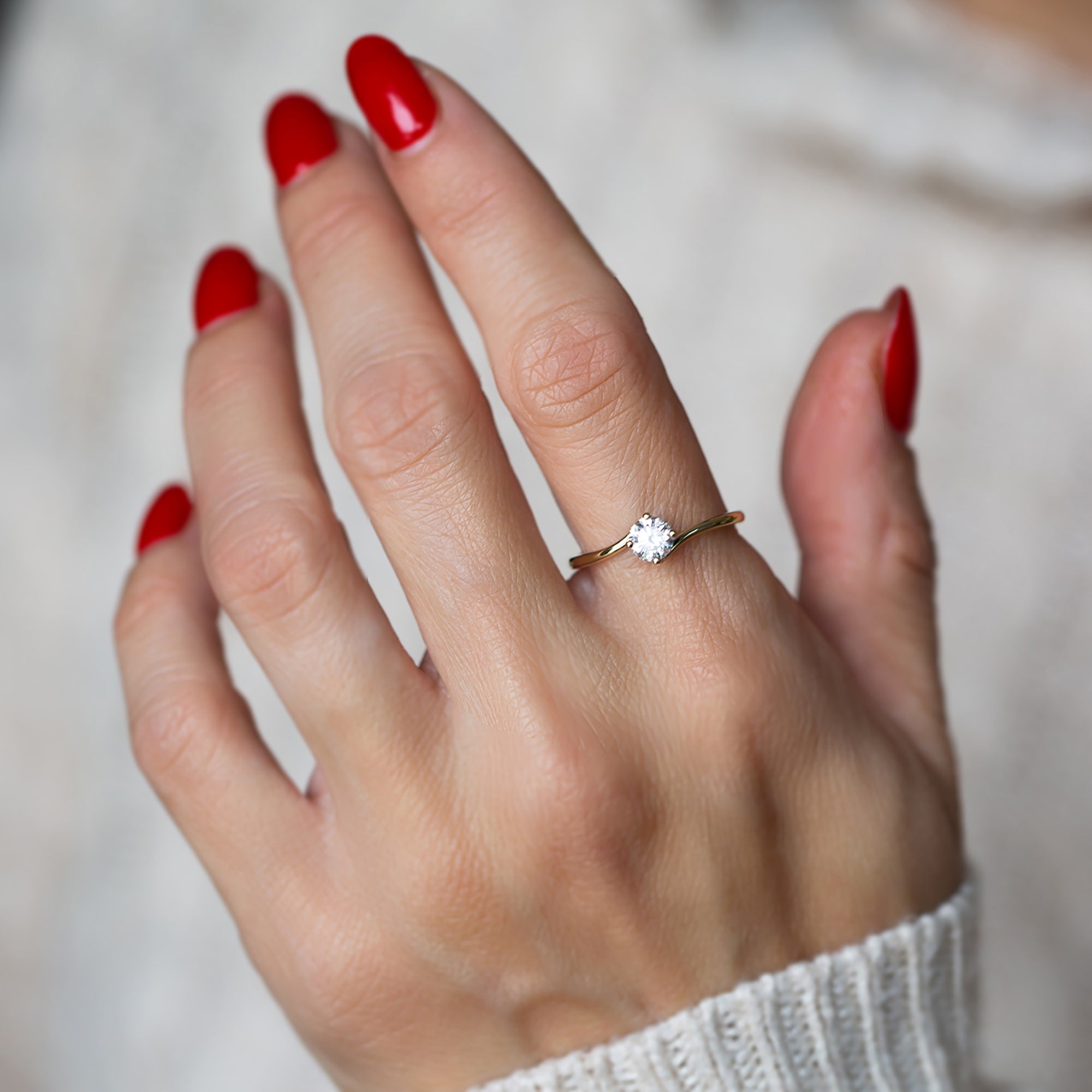 יד של אישה עם לק אדום שעונדת טבעת אירוסין זהב צהוב משובצת יהלום