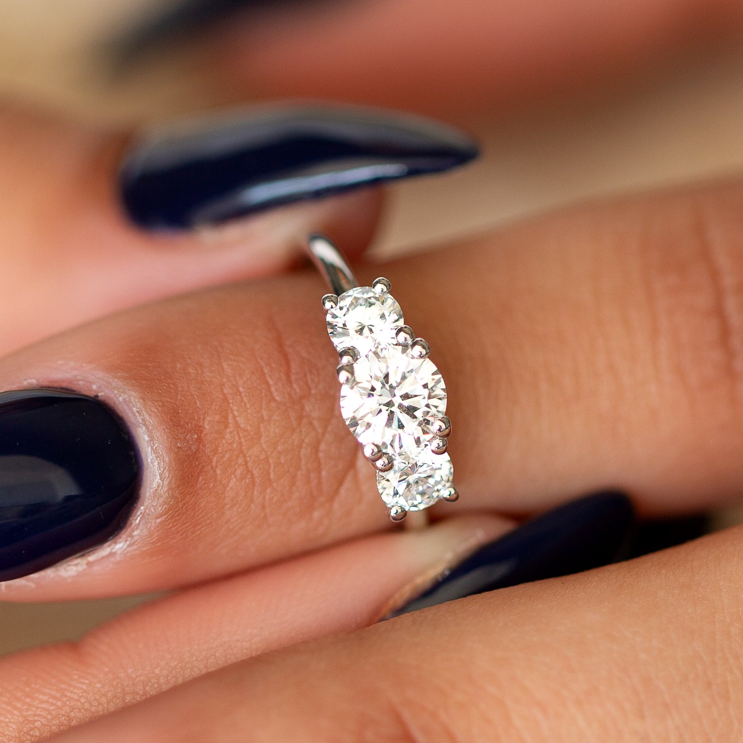 תקריב של יד של אישה עונדת טבעת אירוסין משובצת שלושה יהלומים