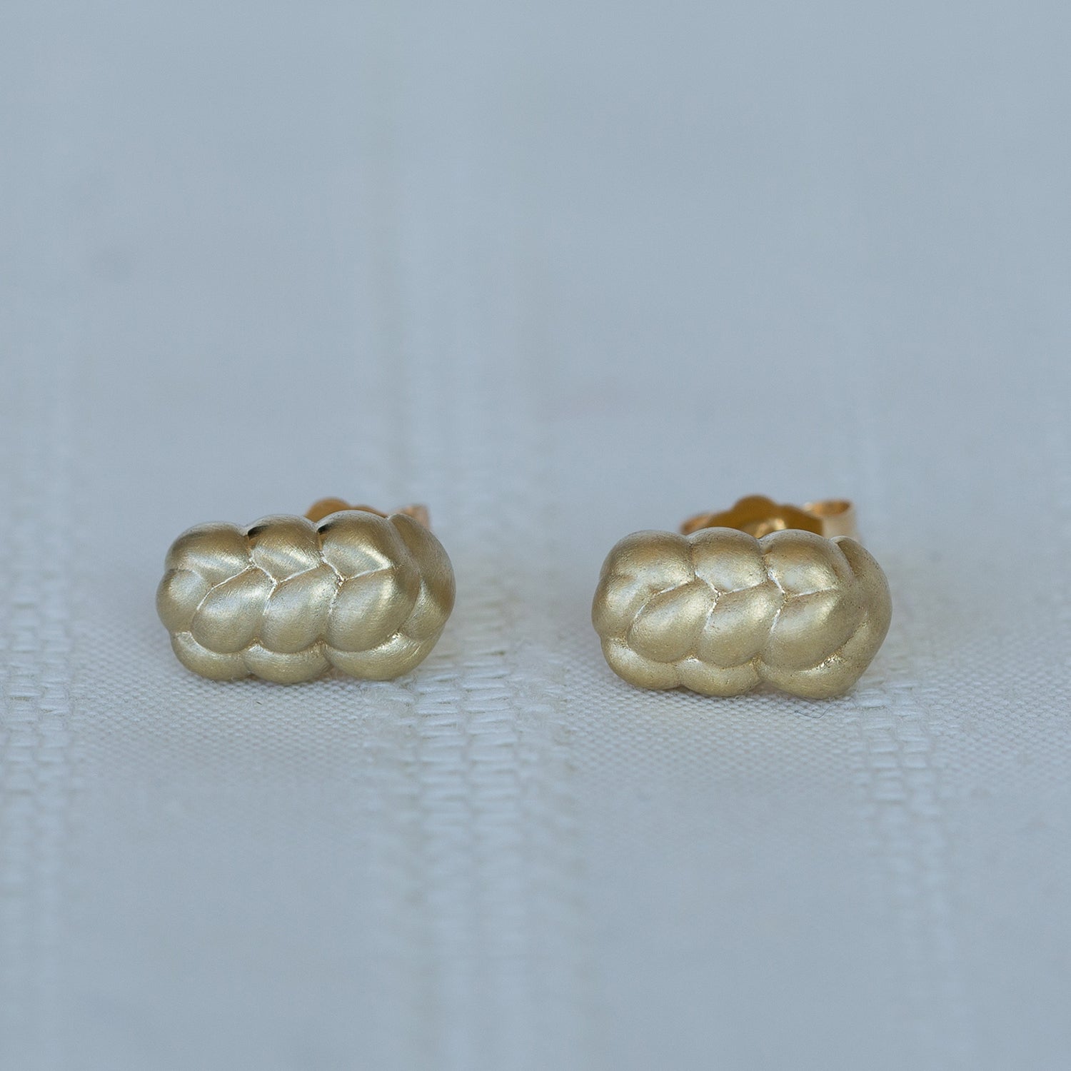 תקריב של זוג עגילי זהב קלועים צמודים על רקע לבן