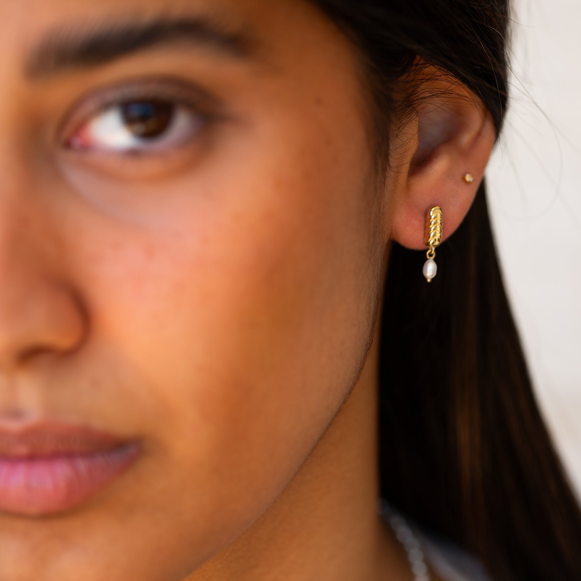 תקריב של פנים של אישה שעונדת עגילים לכלה מזהב משובצים פנינה