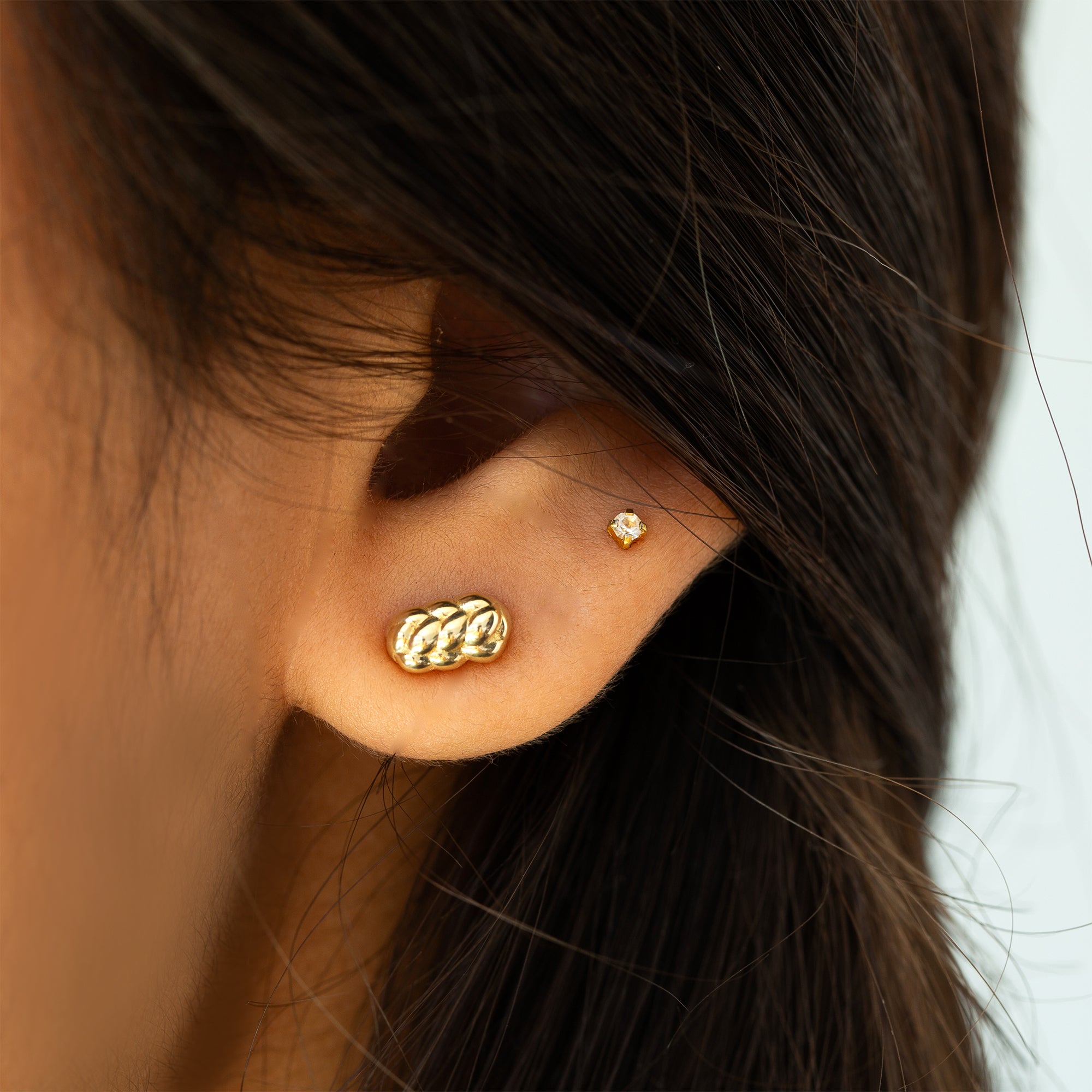 תקריב של אוזן של אישה שעונדת עגיל זהב צהוב 14 קראט בעיצוב קלוע