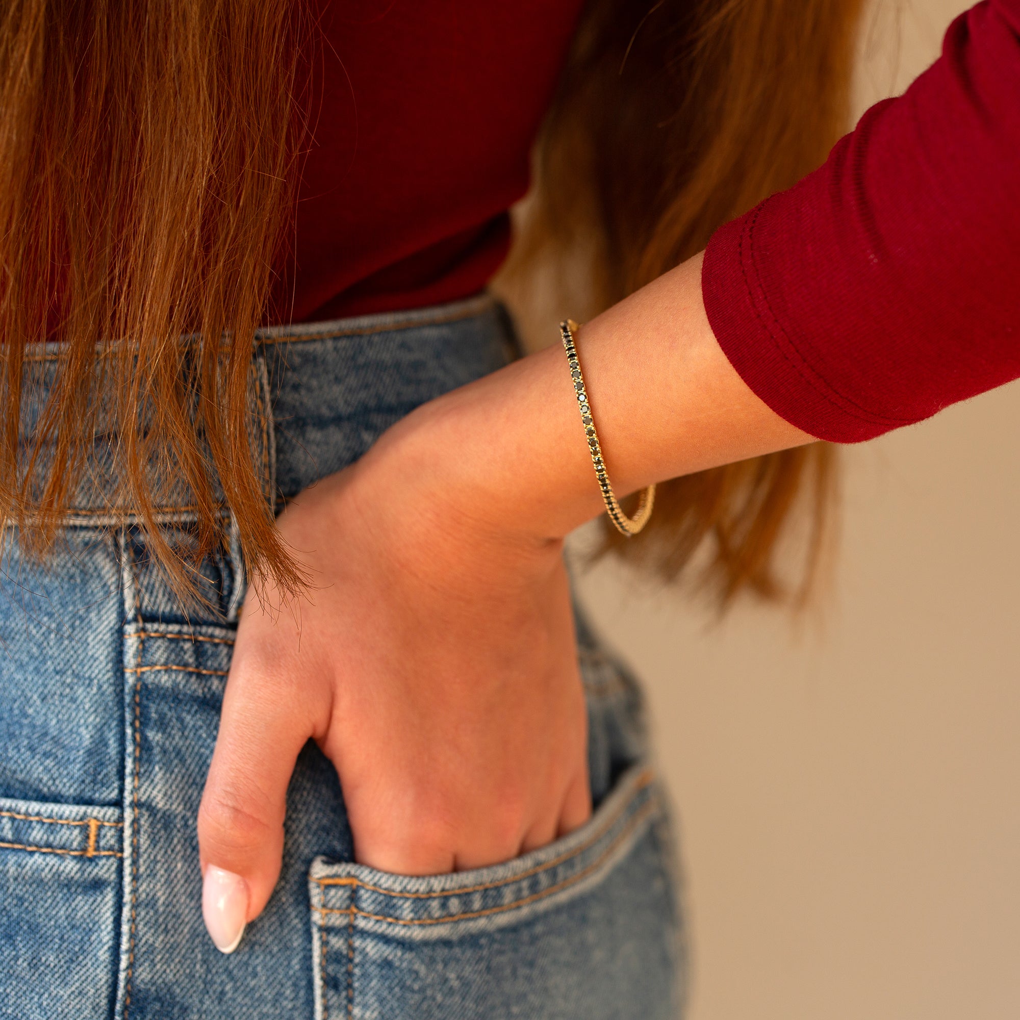 אישה עונדת צמיד זהב 14 קראט משובץ יהלומים שחורים, לובשת ג'ינס כחול וחולצה אדומה