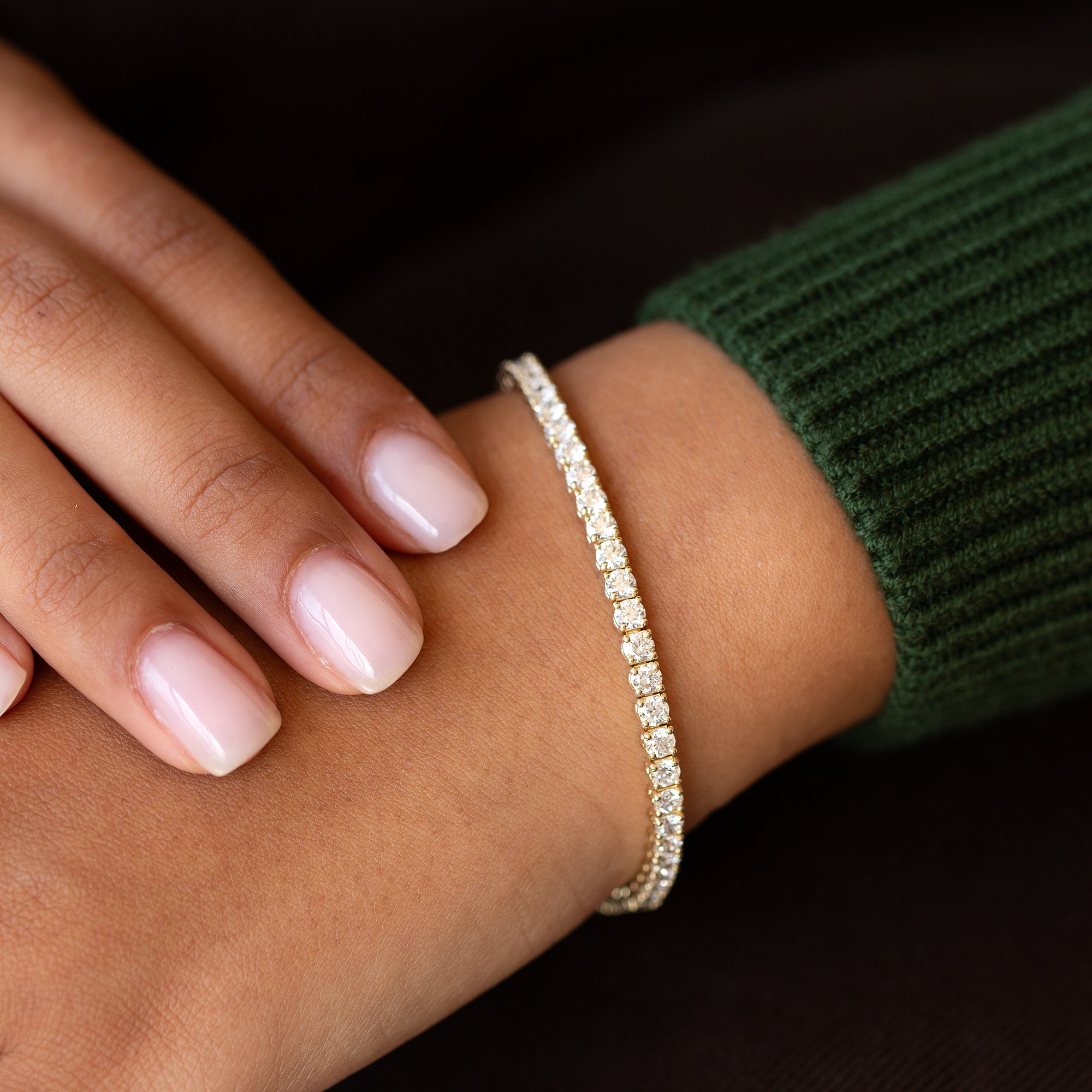 תקריב של יד של אישה עונדת צמיד טניס מושבץ יהלומים לבנים