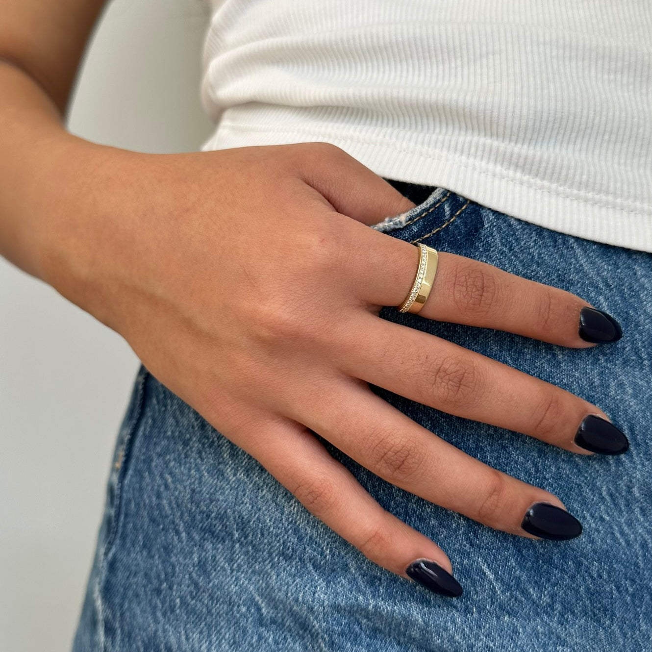 תקריב של יד של אישה שעונדת טבעת זהב צהוב 14K משובצת שורת יהלומים לבנים