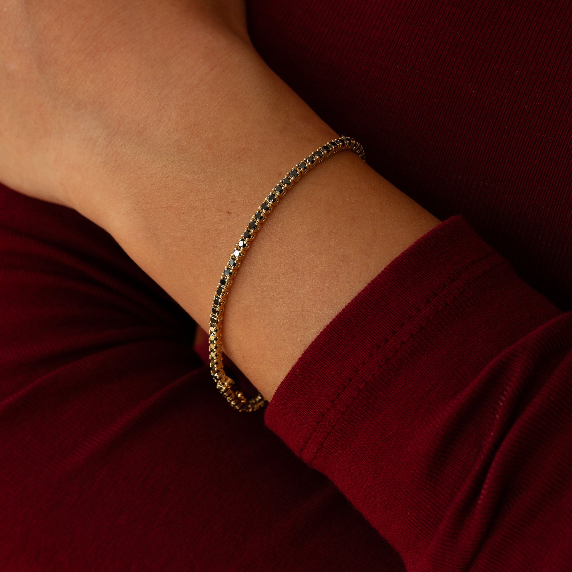 פרק יד של אישה שעונדת צמיד משובץ יהלומים שחורים בזהב 14 קראט על רקע אדום