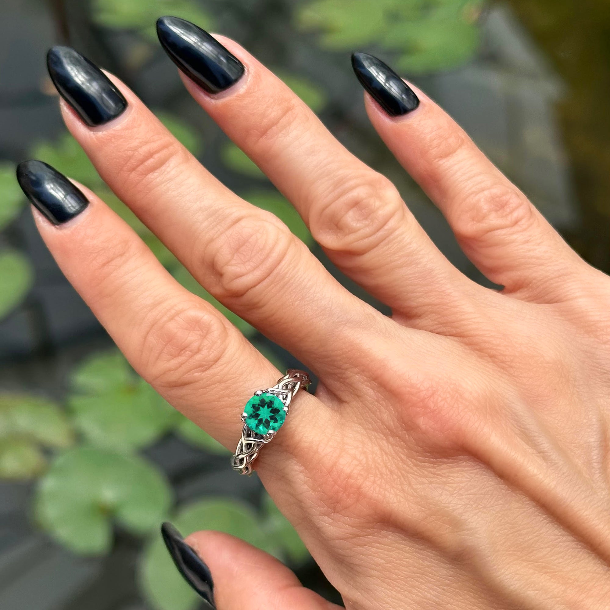 יד של אישה עם לק שחור שעונדת טבעת אירוסין אמרלד