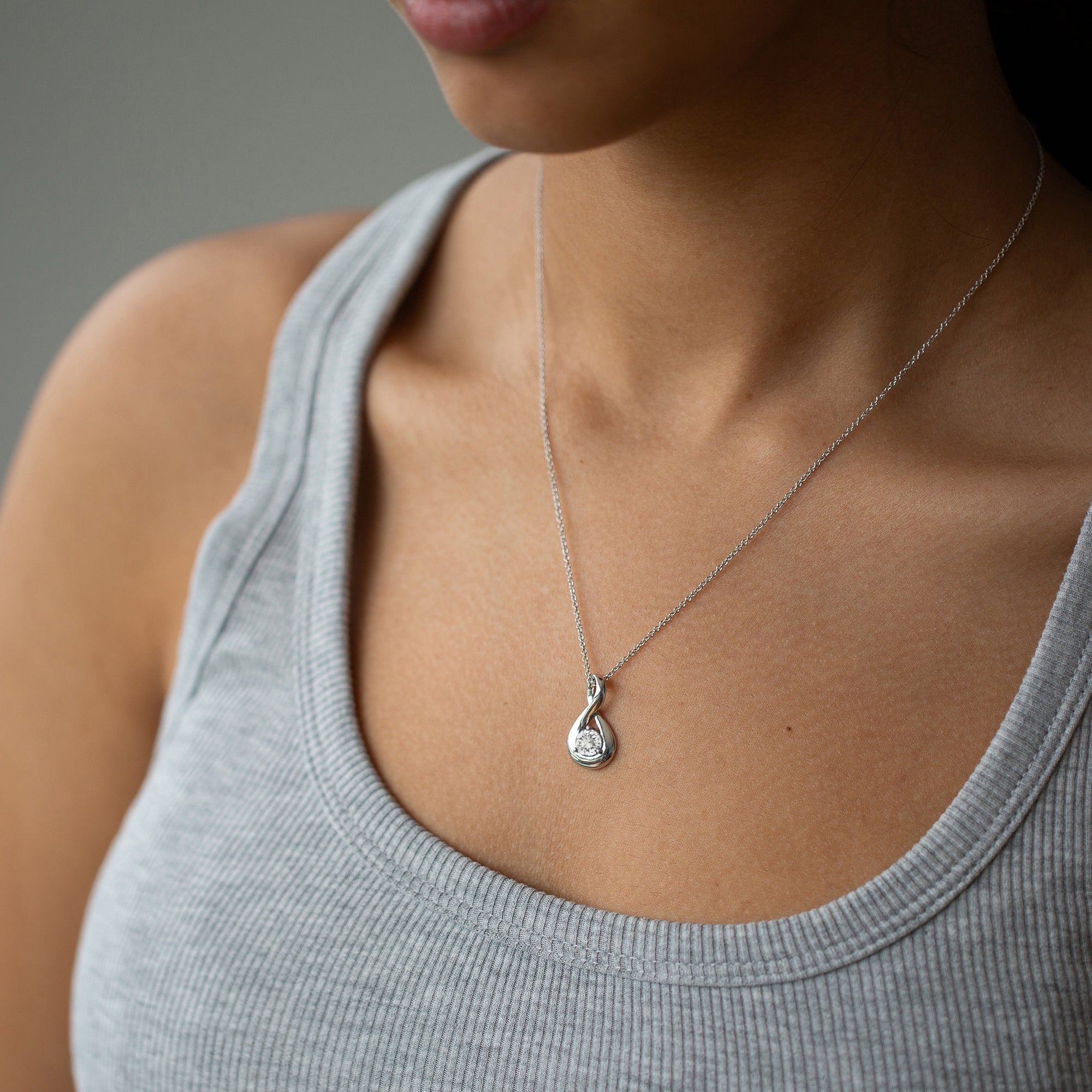 אישה עונדת שרשרת זהב לבן עם תליון משובץ יהלום וגופיה אפורה