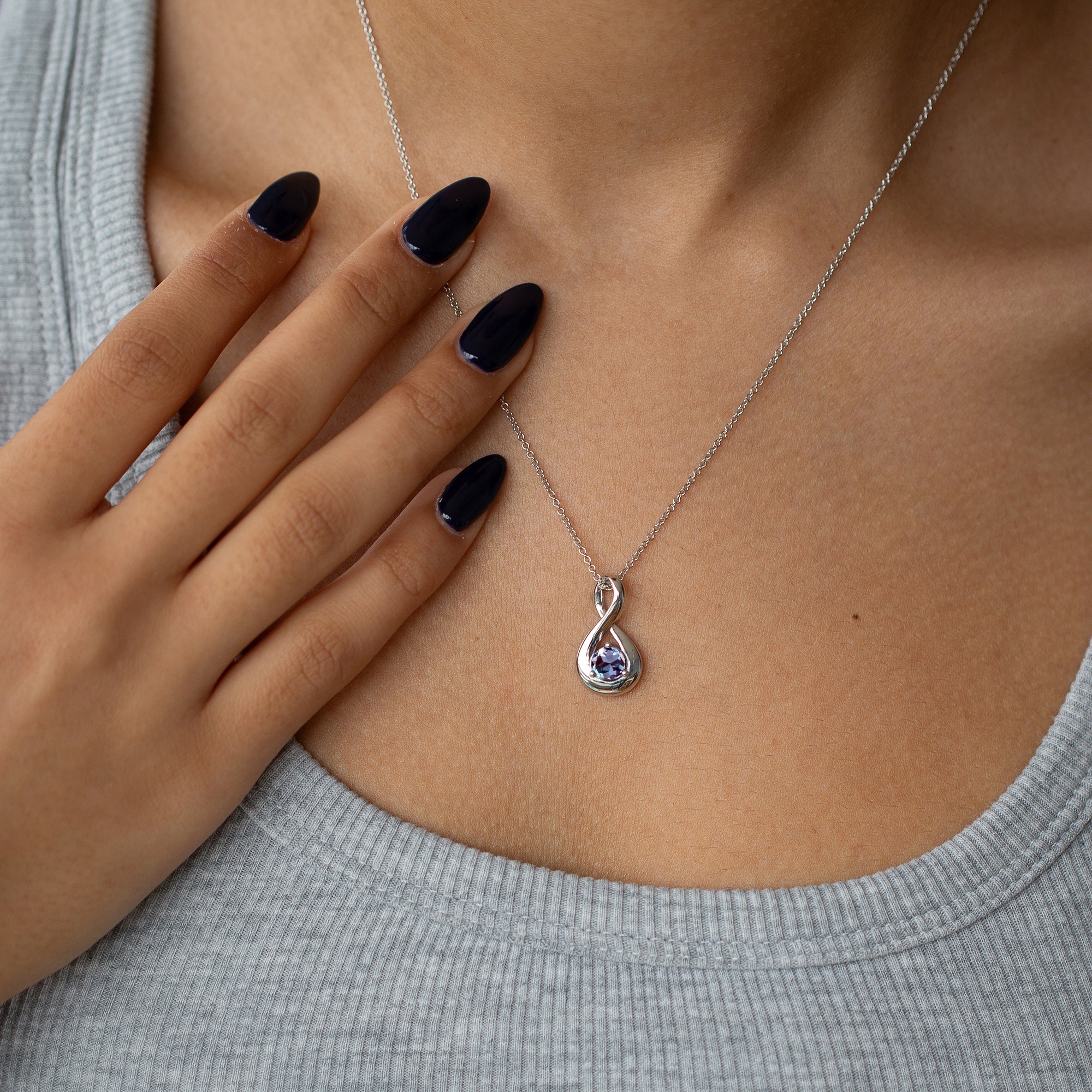 אישה עונדת שרשרת אינפיניטי בזהב לבן משובצת אבן חן כחולה עם חולצה אפורה