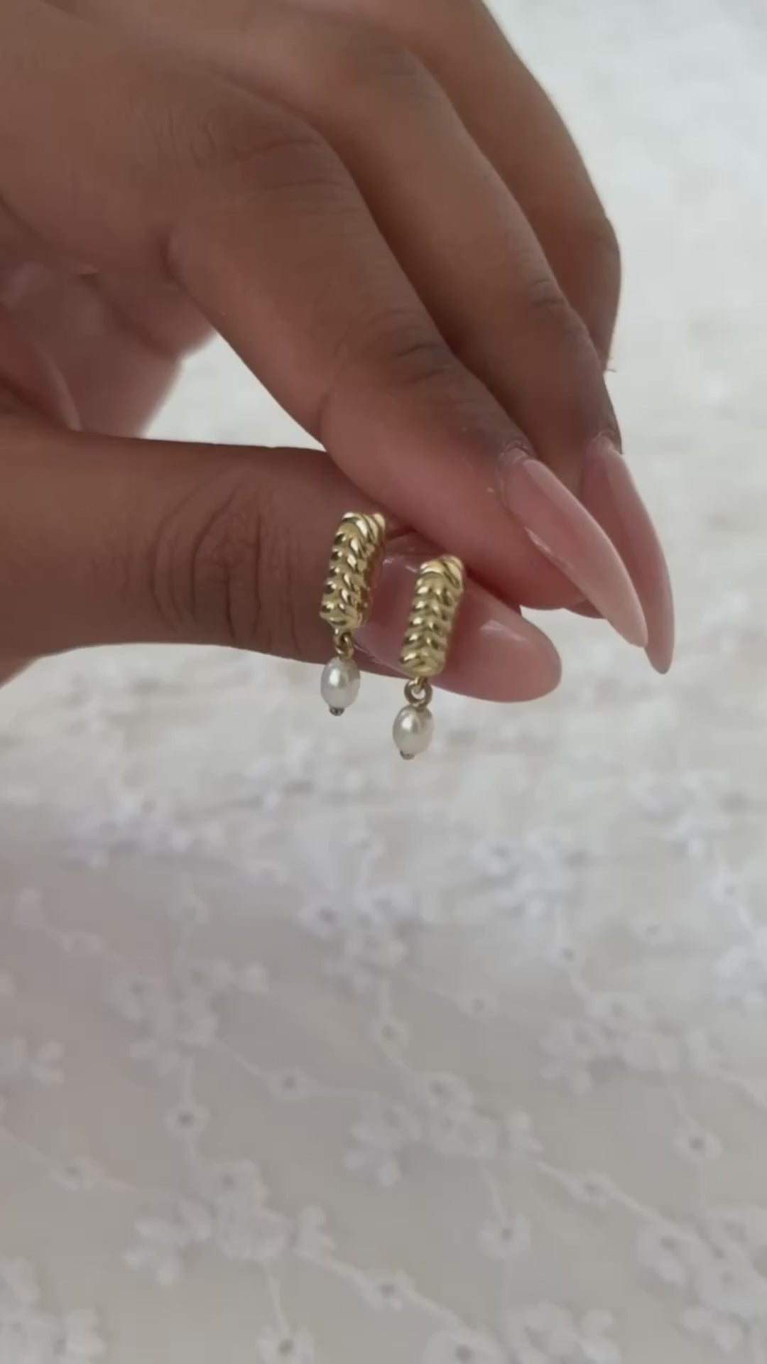 תקריב של יד שמחזיקה עגילי זהב משובצים פנינה בעיצוב קלוע