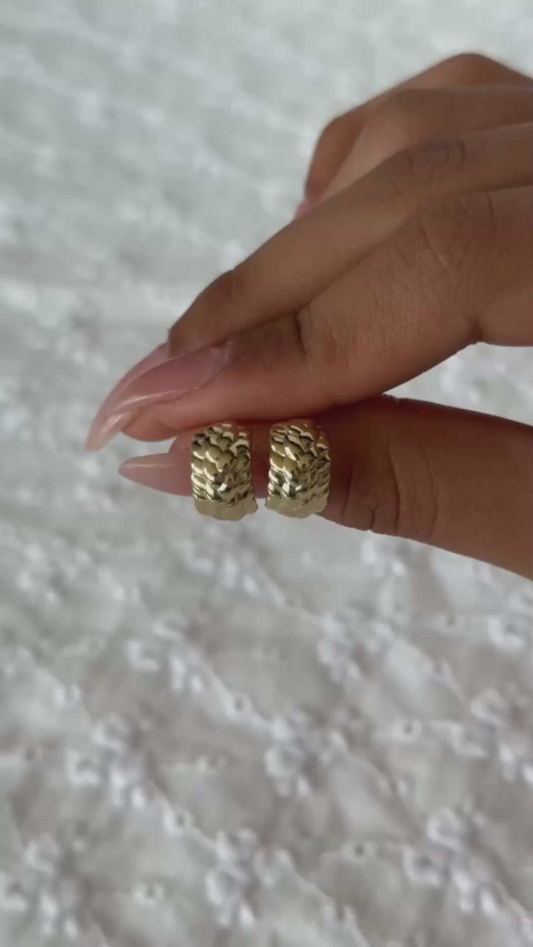 תקריב של יד שמחזיקה זוג עגילי חישוק זהב 14K עם טקסטורה קלועה