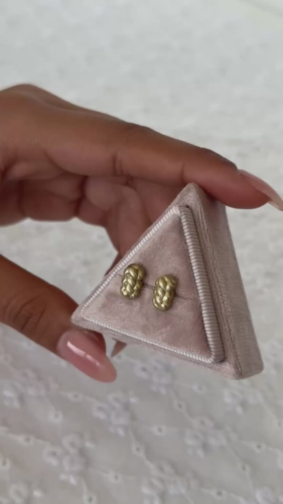 עגילי זהב קלועים צמודים בזהב צהוב מוחזקים על ידי יד של אישה בתוך קופסת תכשיטים