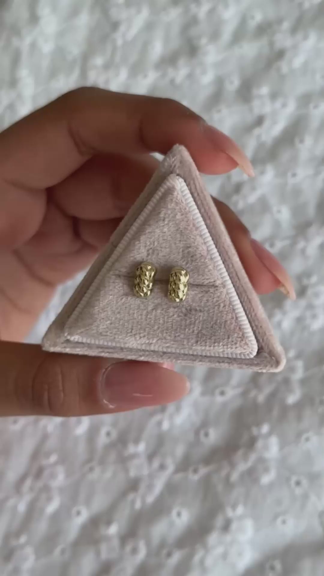 יד של אישה שמחזיקה קופסת עגילים משולשת עם עגילי זהב צמודים