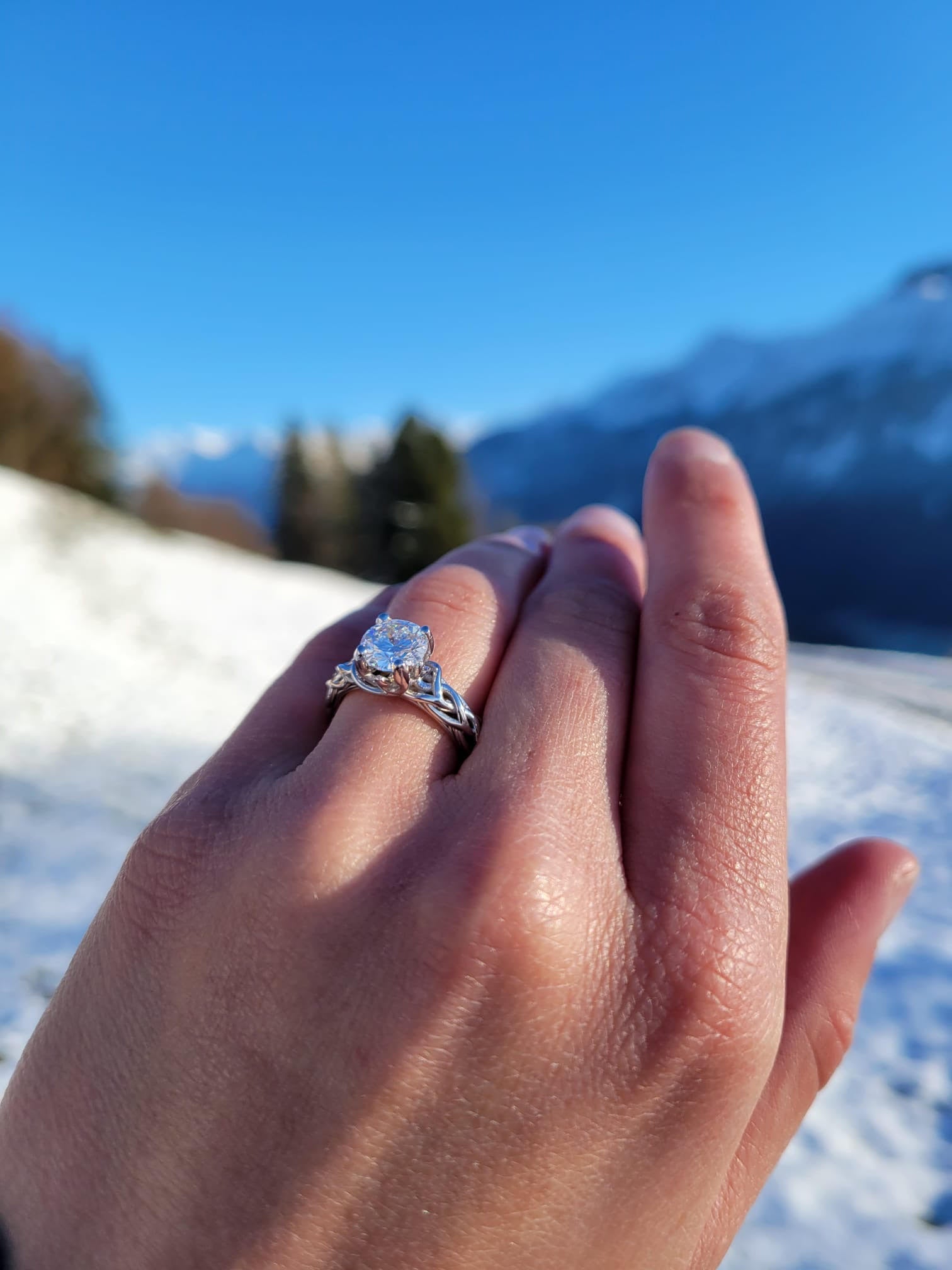 יד של אישה שעונדת טבעת מואסנייט מרשימה משובצת על רקע מושלג