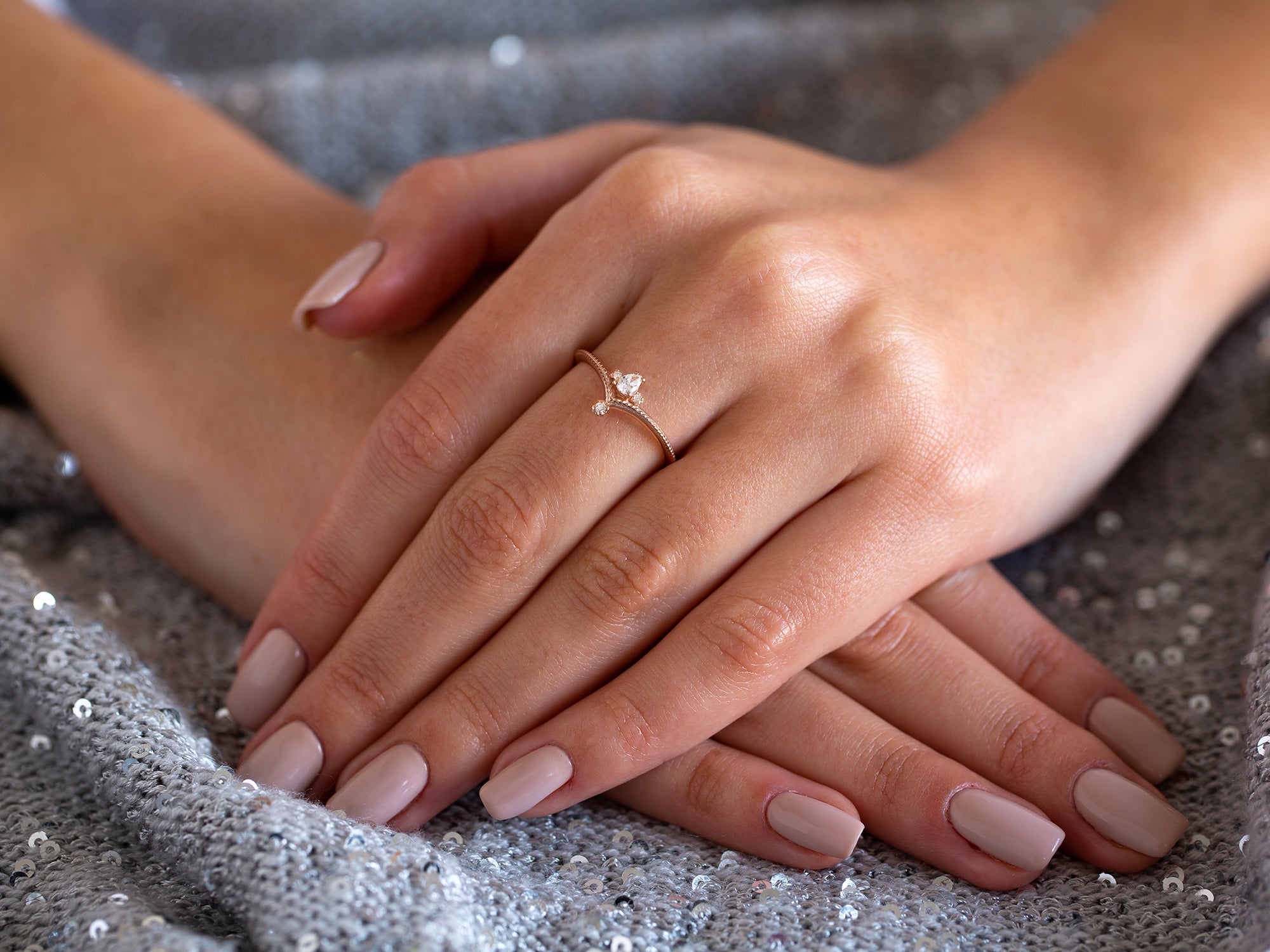 ידיים של אישה שעונדת טבעת אירוסין טיפה בזהב אדום על רקע בד אפור