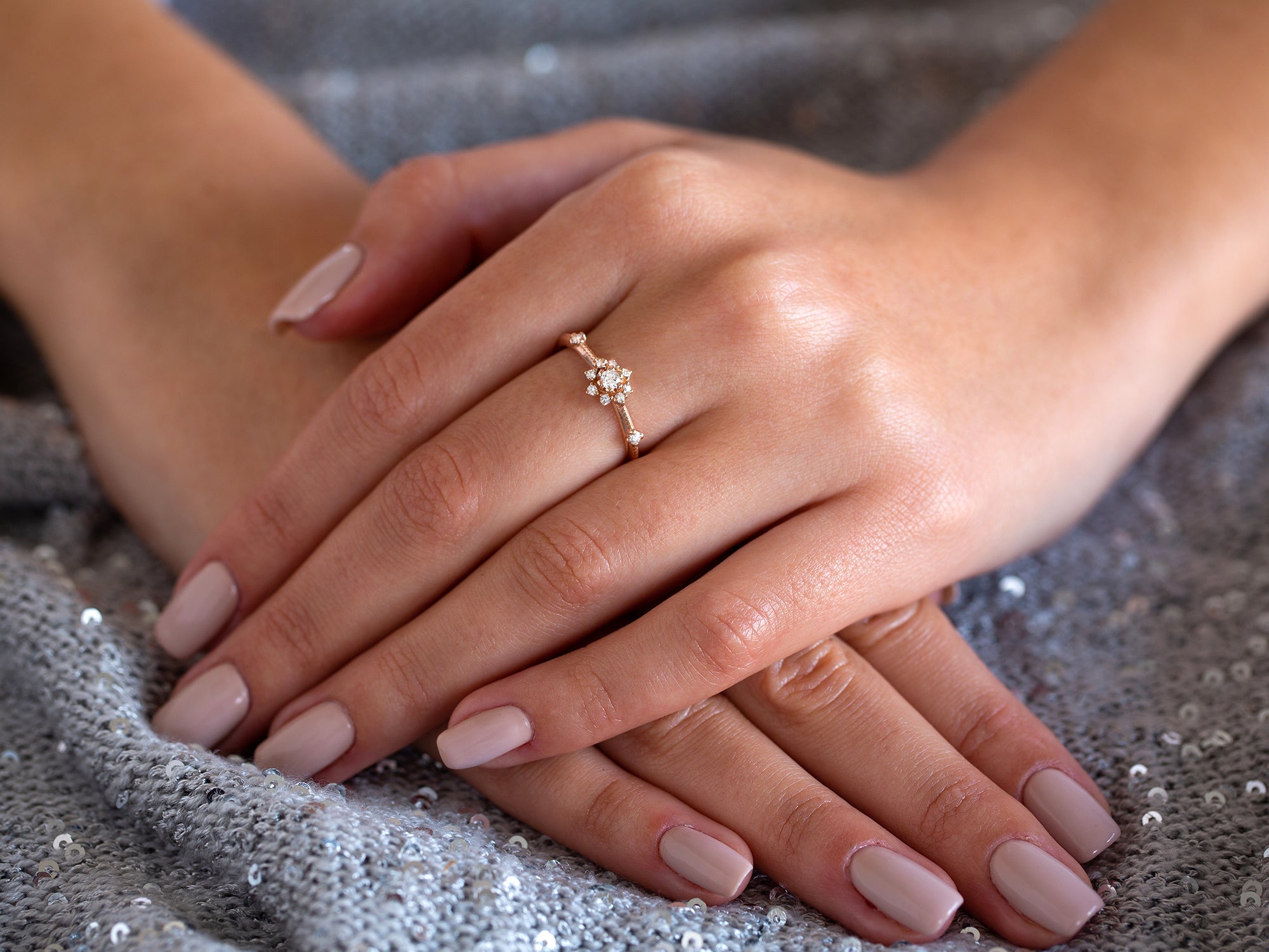 ידיים של אישה שעודת טבעת פרח יהלומים בזהב על רקע אפור