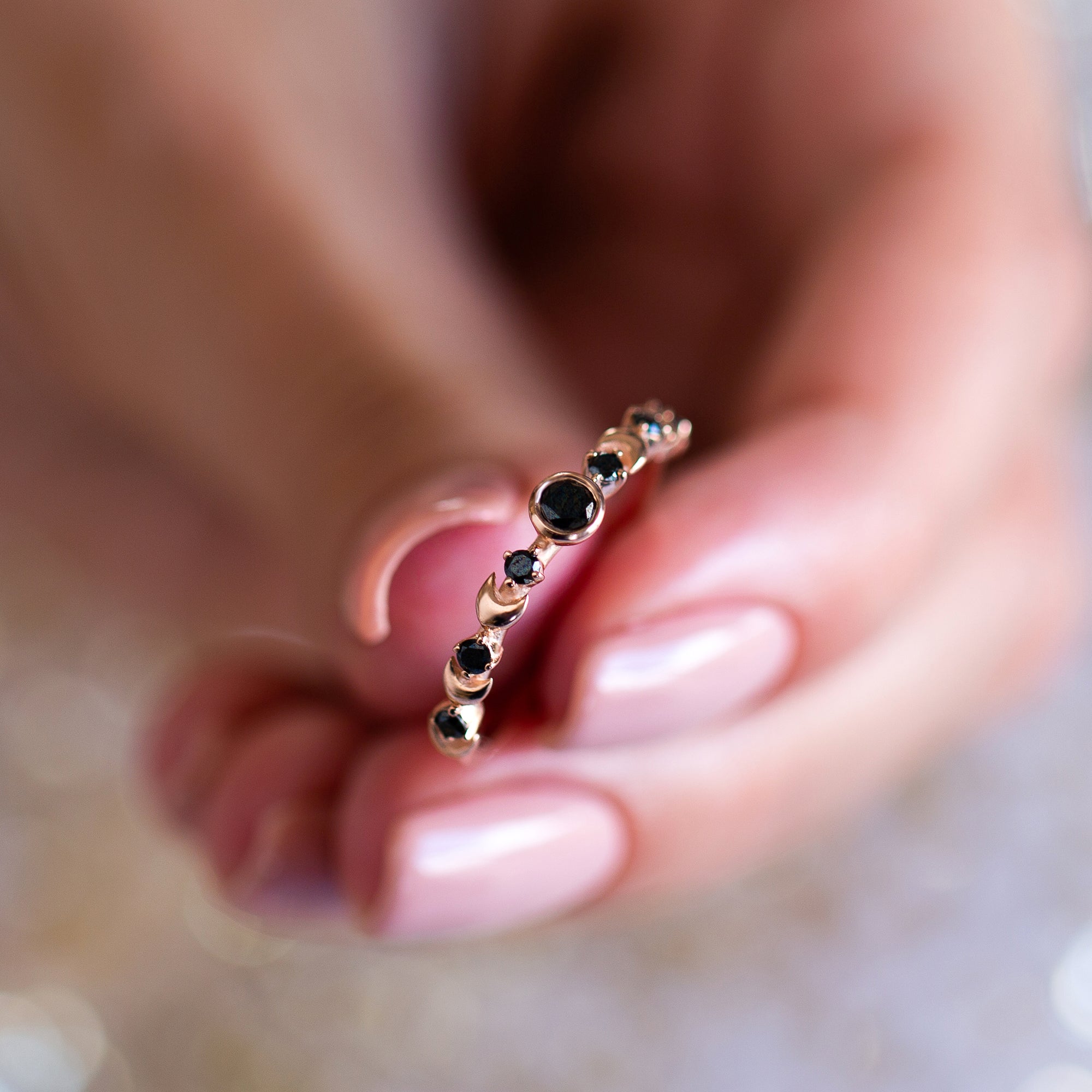 אצבעות של אישה מחזיקות טבעת זהב עדינה משובצת יהלומים שחורים