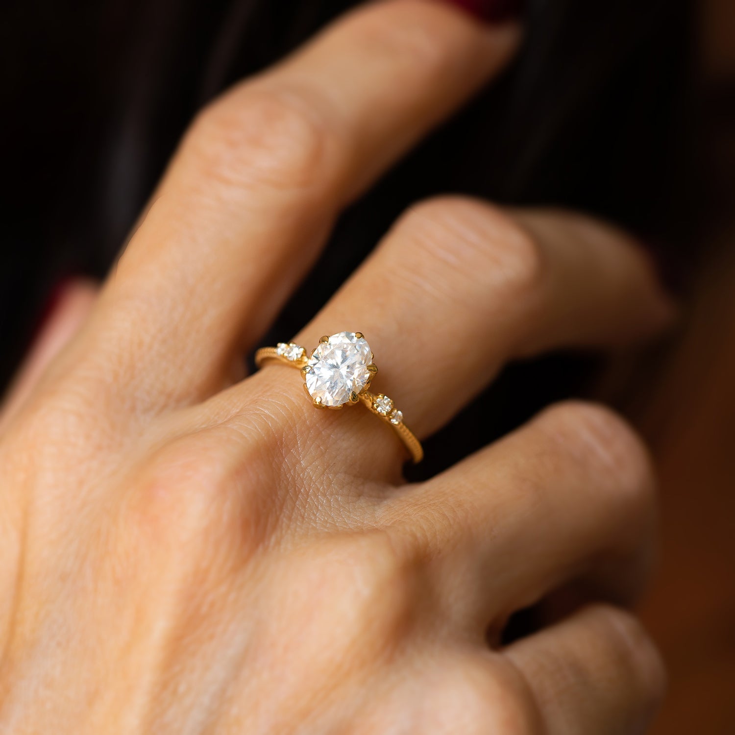 אישה עונדת טבעת אירוסין זהב צהוב 14 קראט משובצת מואסנייט ויהלומים עדינים בצדדים