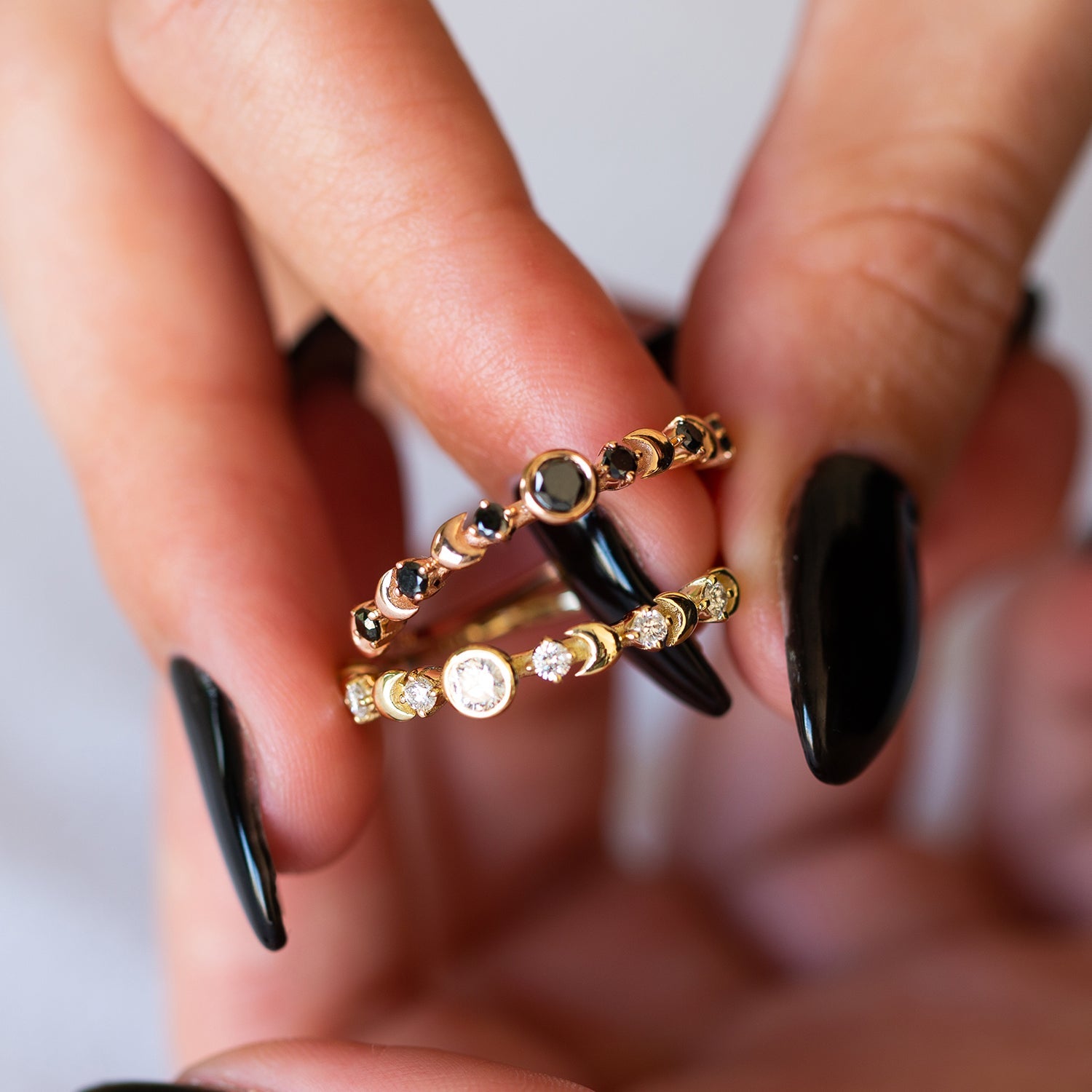 אצבעות של אישה שמחזיקות זוג טבעות זהב מיוחדות משובצות יהלומים לבנים ושחורים