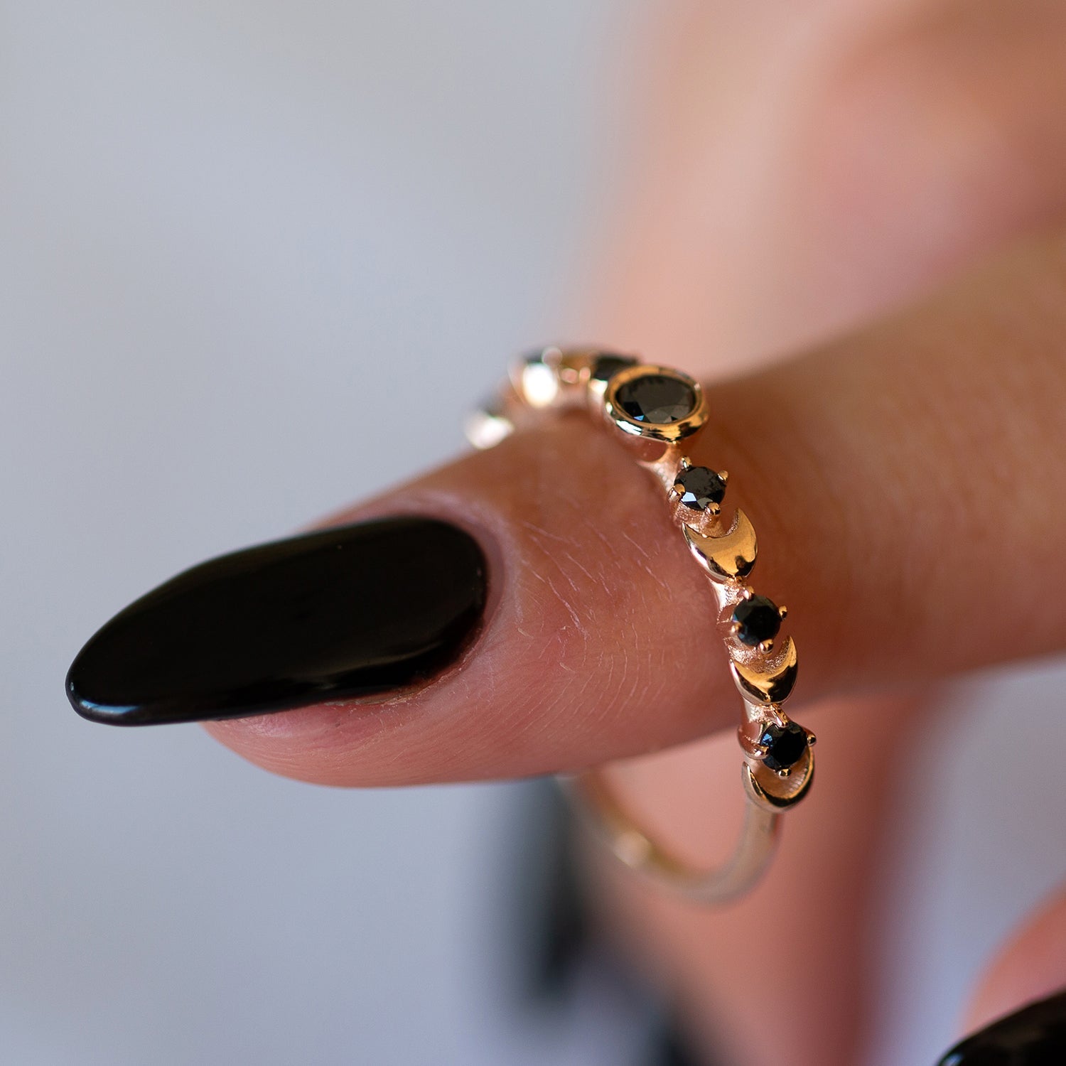 אצבע של אישה שתלויה עליה טבעת ירח מזהב משובצת יהלומים שחורים