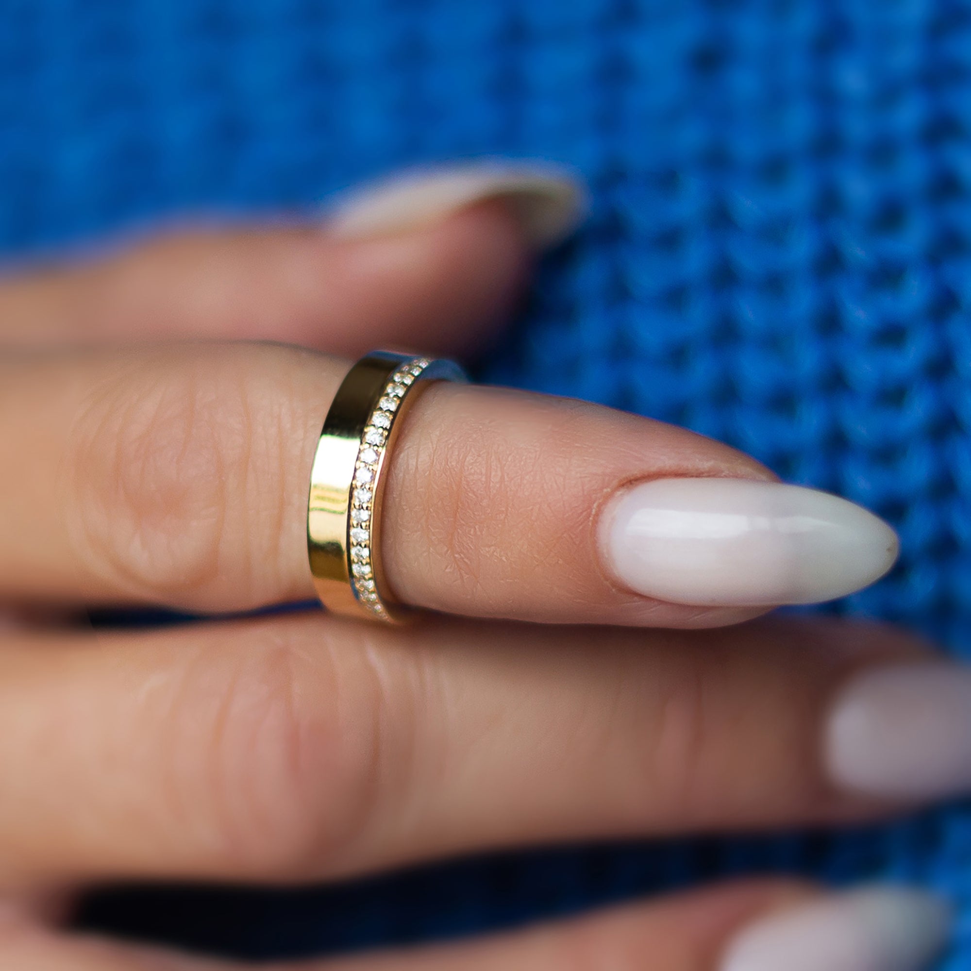 תקריב של אצבע של אישה שעונדת טבעת יהלומים שורה בזהב צהוב עם רקע כחול