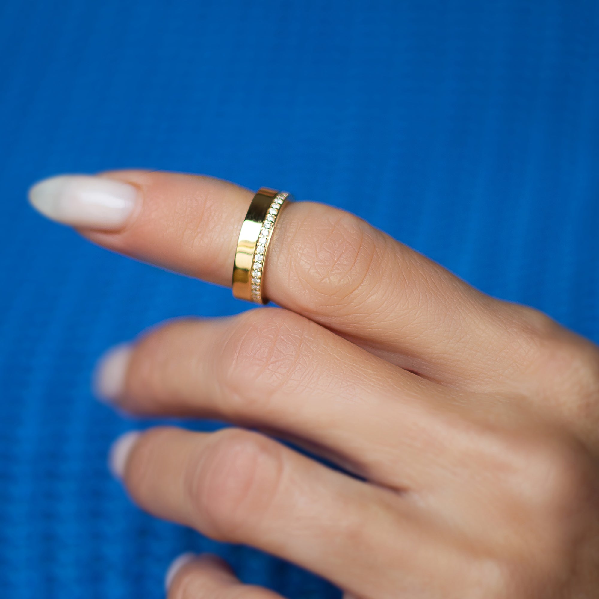 אצבע של אישה שעונדת טבעת זהב רחבה משובצת שורת יהלומים לבנים