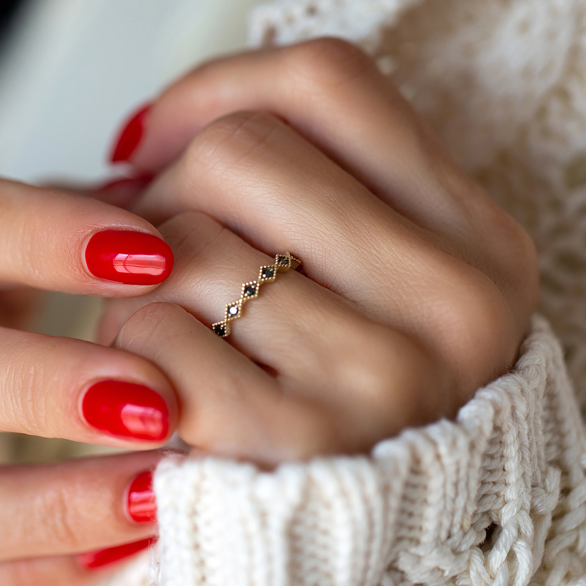 אישה עונדת טבעת איטרניטי זהב משובצת יהלומים שחורים בעיצוב מעויינים