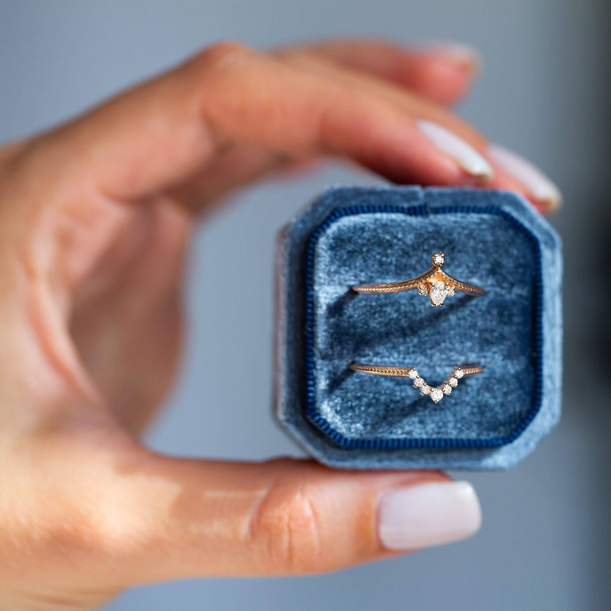 אישה מחזיקה קופסת תכשיטים כחולה ובתוכה טבעות זהב אדום עדינות משובצות יהלומי מעבדה