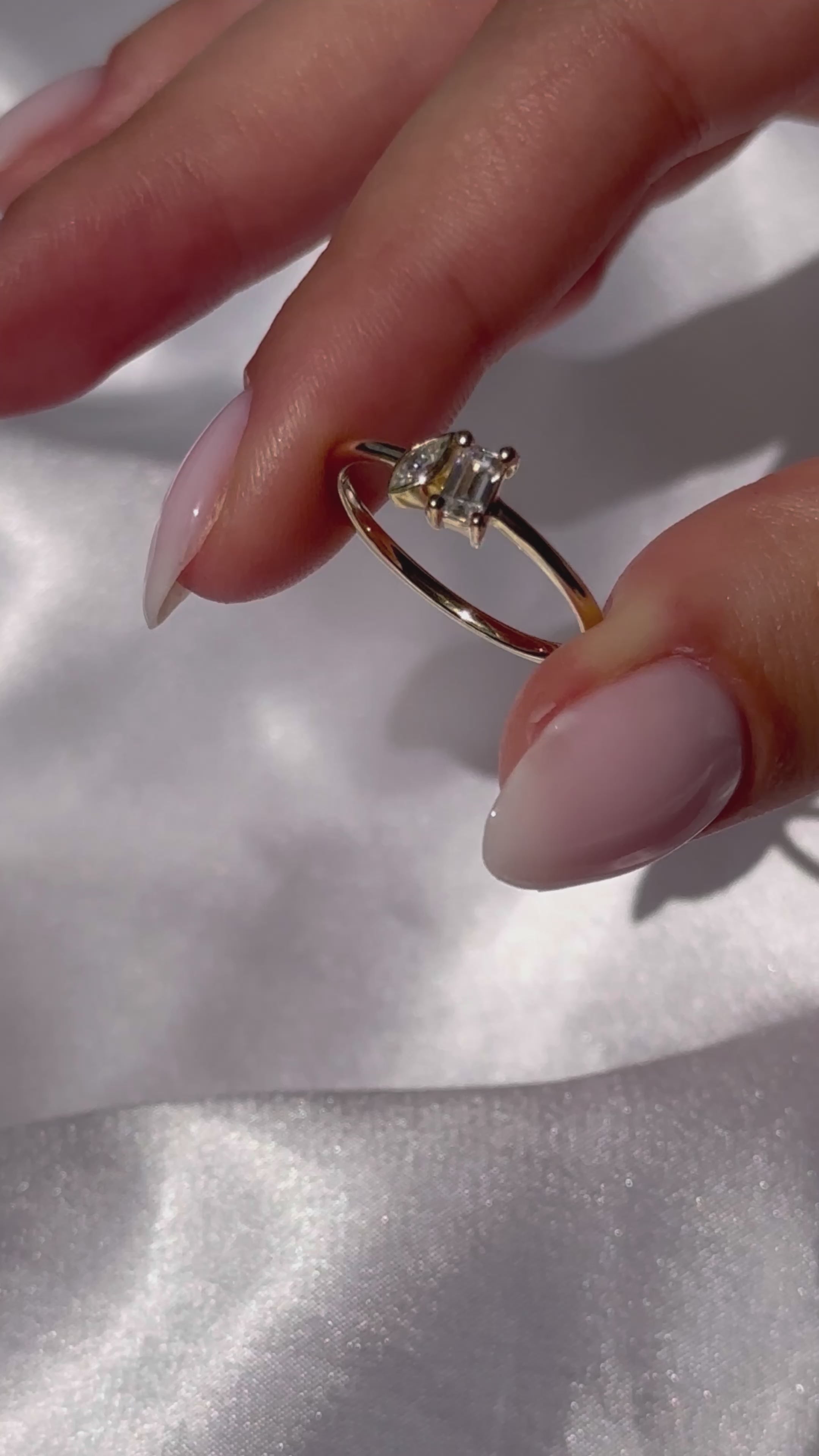 טבעת יהלום מעבדה עדינה משובצת יהלומים בחיתוך מרקיזה ואמרלד בזהב צהוב, שמחזיקה אותה יד של אישה