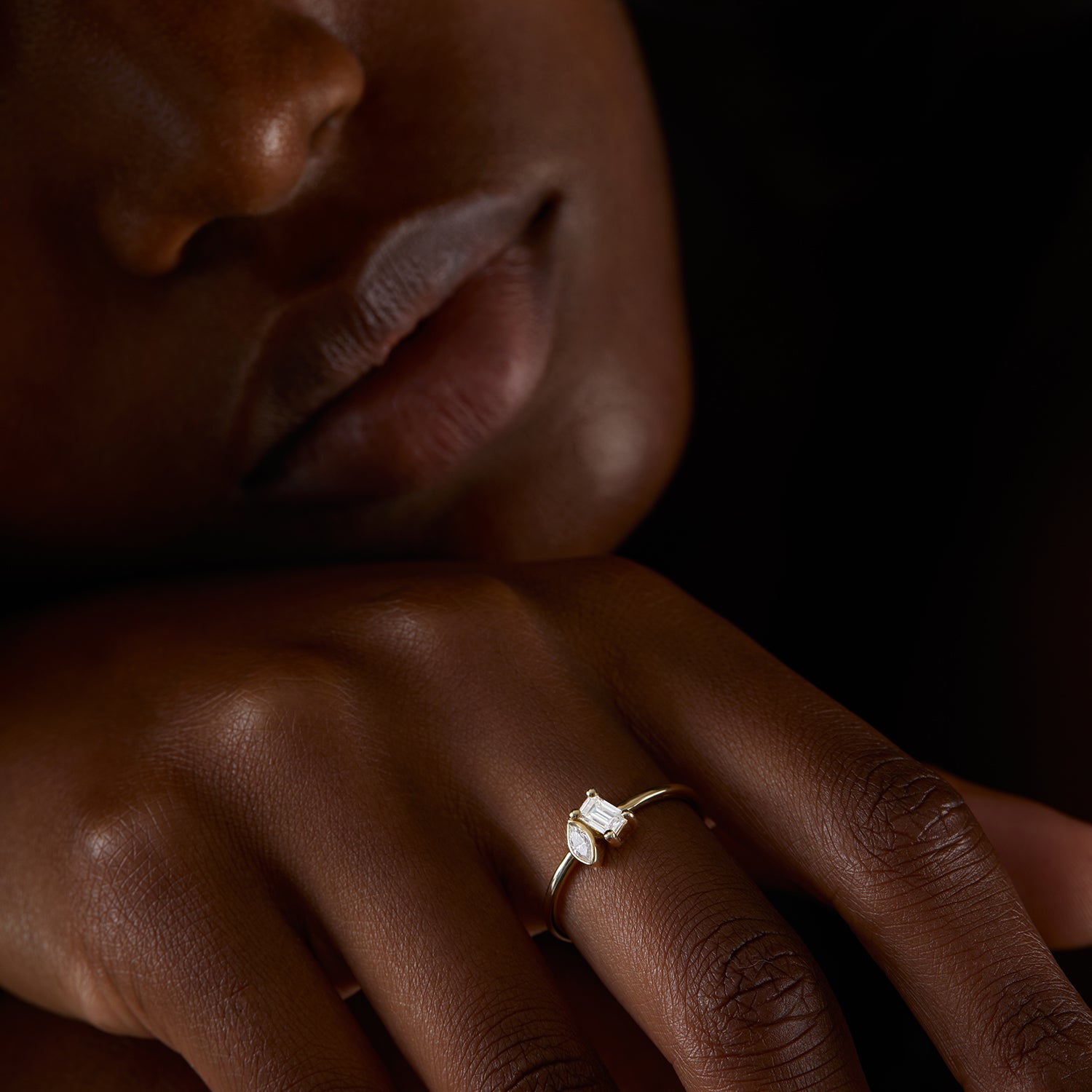 חלק תחתון של פנים של אישה וחלק מהיד שלה שעונדת טבעת מואסנייט עדינה משובצת שתי אבנים בזהב צהוב