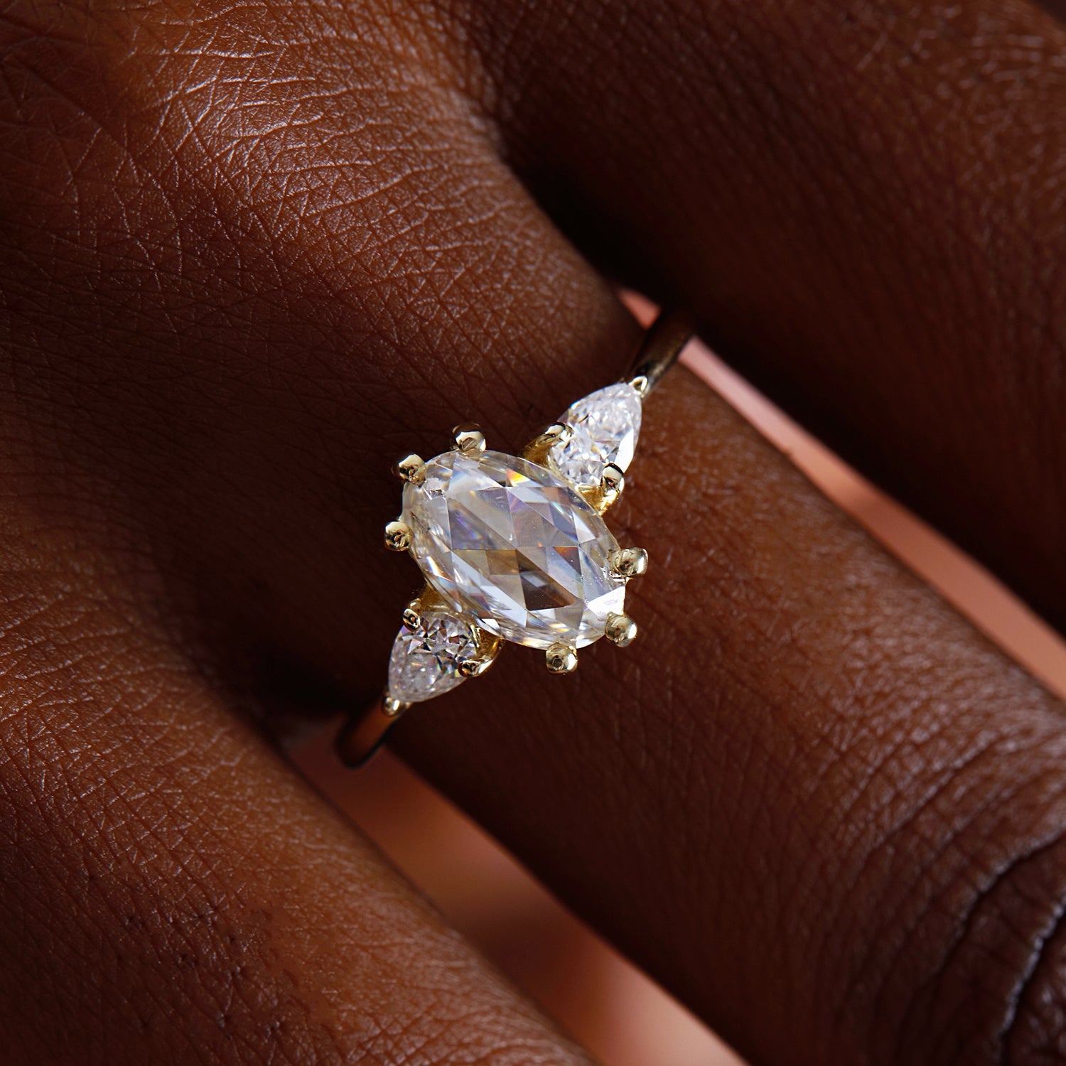 תקריב של אצבע של אישה שעונדת טבעת זהב אובלית משובצת יהלומי טיפה