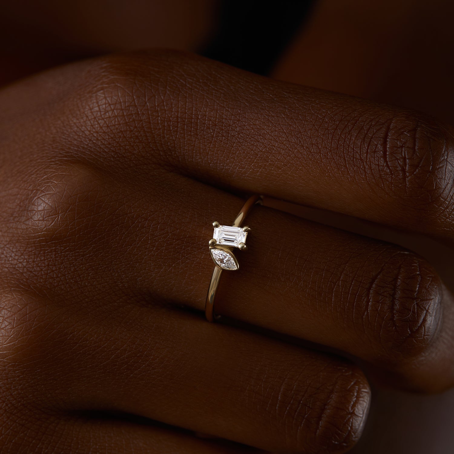 תקריב של יד של אישה שעונדת טבעת זהב צהוב 14 קראט משובצת יהלומי מעבדה בחיתוך אמרלד ומרקיזה