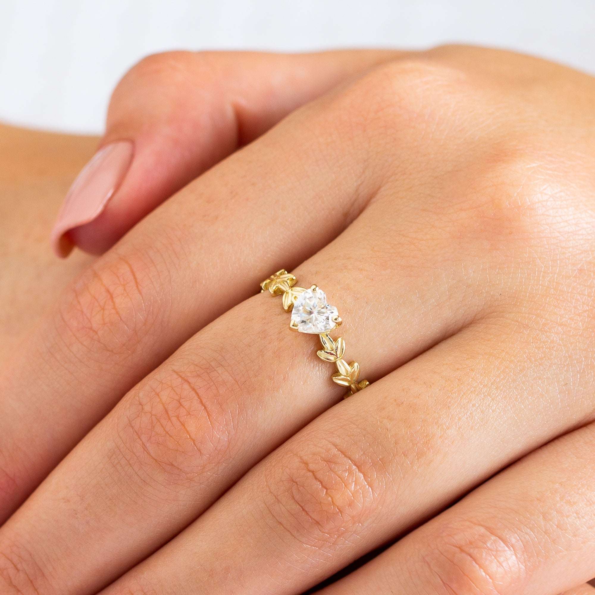 תקריב של יד של אישה שעונדת טבעת עלים מזהב משובצת יהלום לב