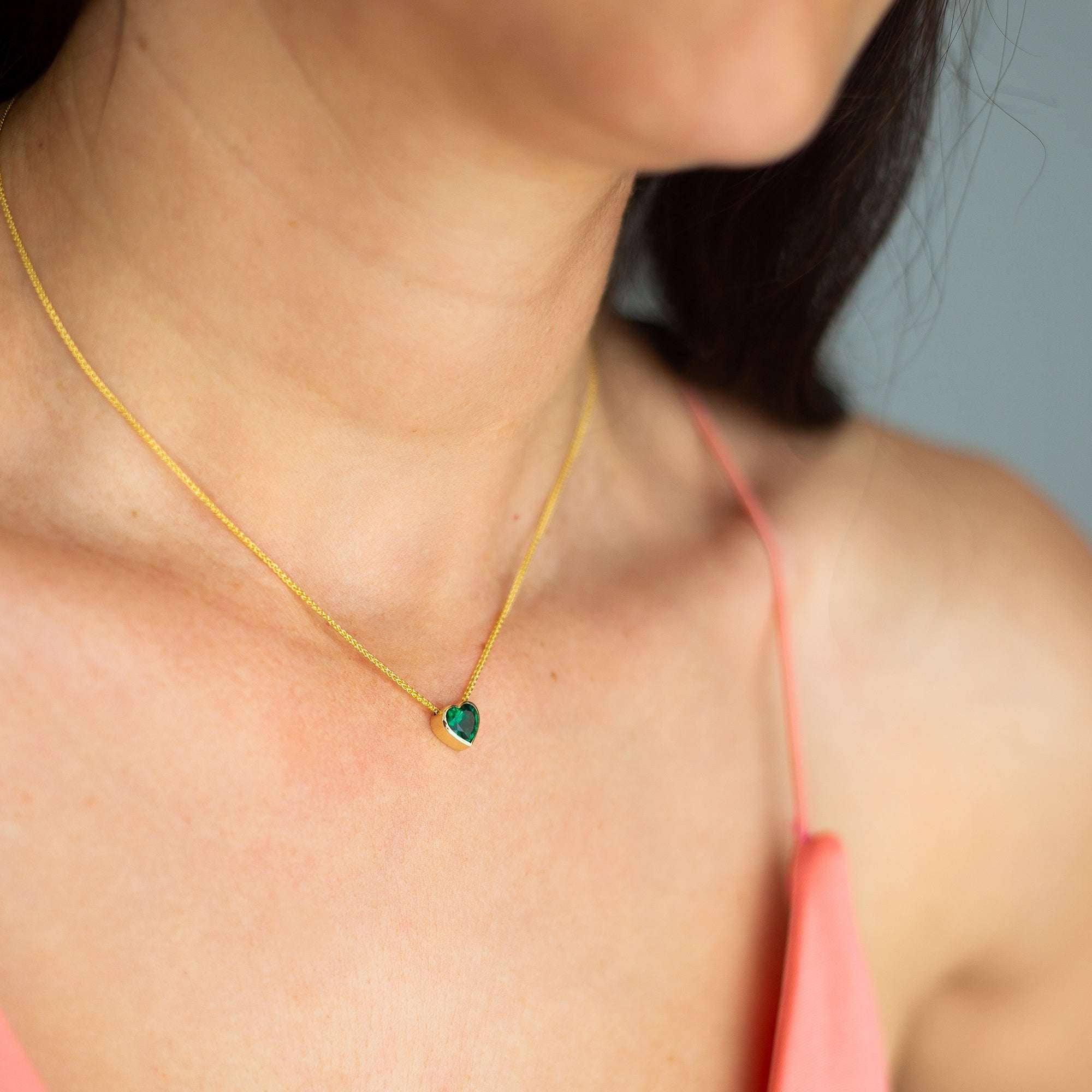 תקריב של צוואר של אישה שעונדת שרשרת אמרלד בצורת לב, עשויה זהב 14 קראט