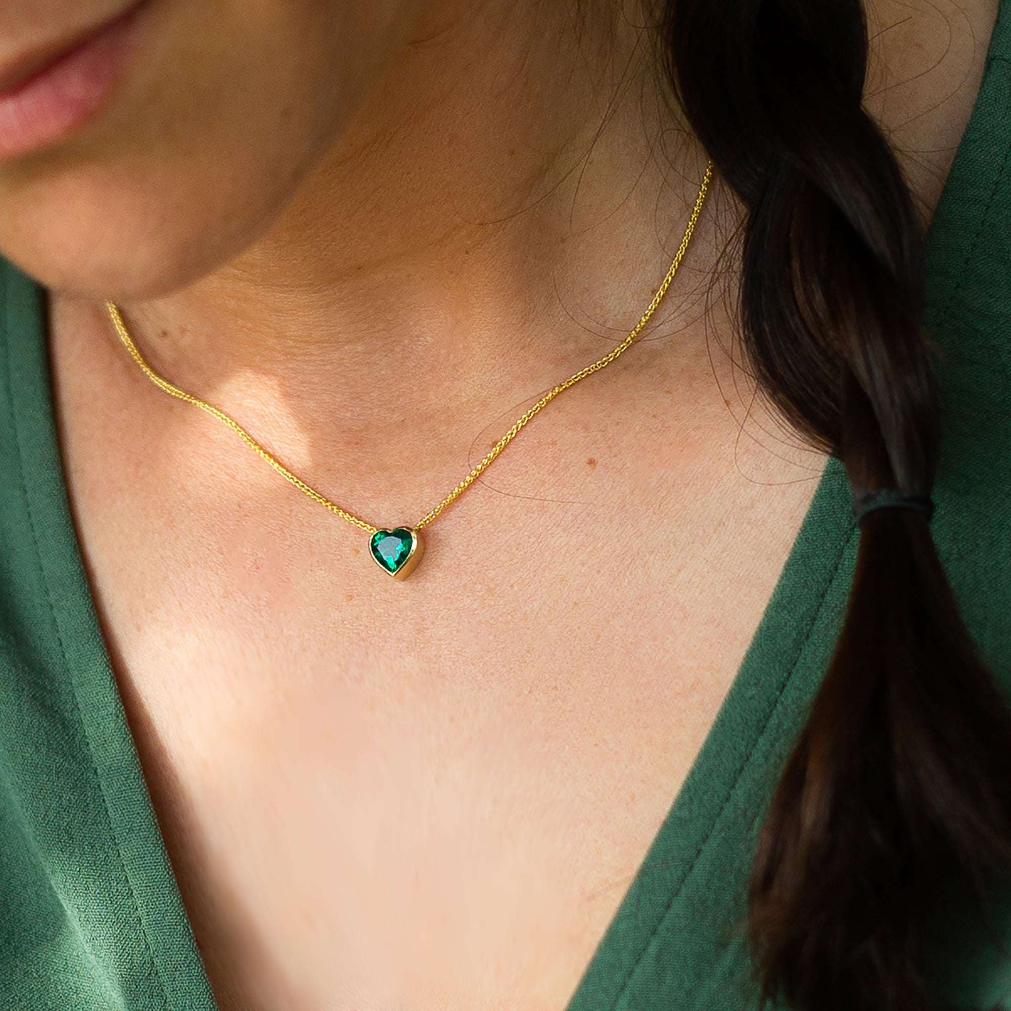 תקריב של צוואר של אישה שעונדת תליון לב משובץ באמרלד על שרשרת זהב
