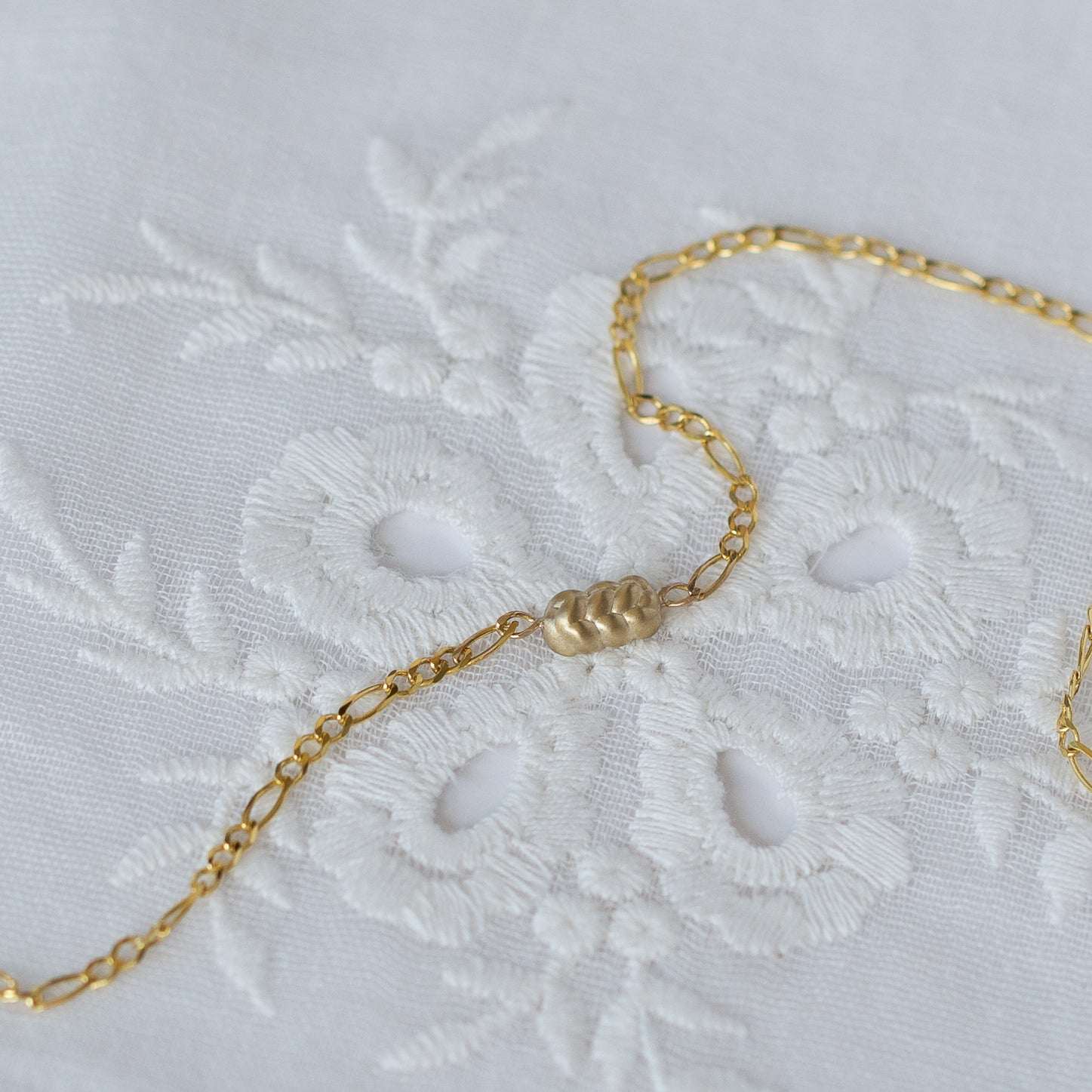 שרשרת זהב רחבה לאישה ובמרכזה תליון בצורת חלה בזהב צהוב 14 קראט על רקע בד רקום