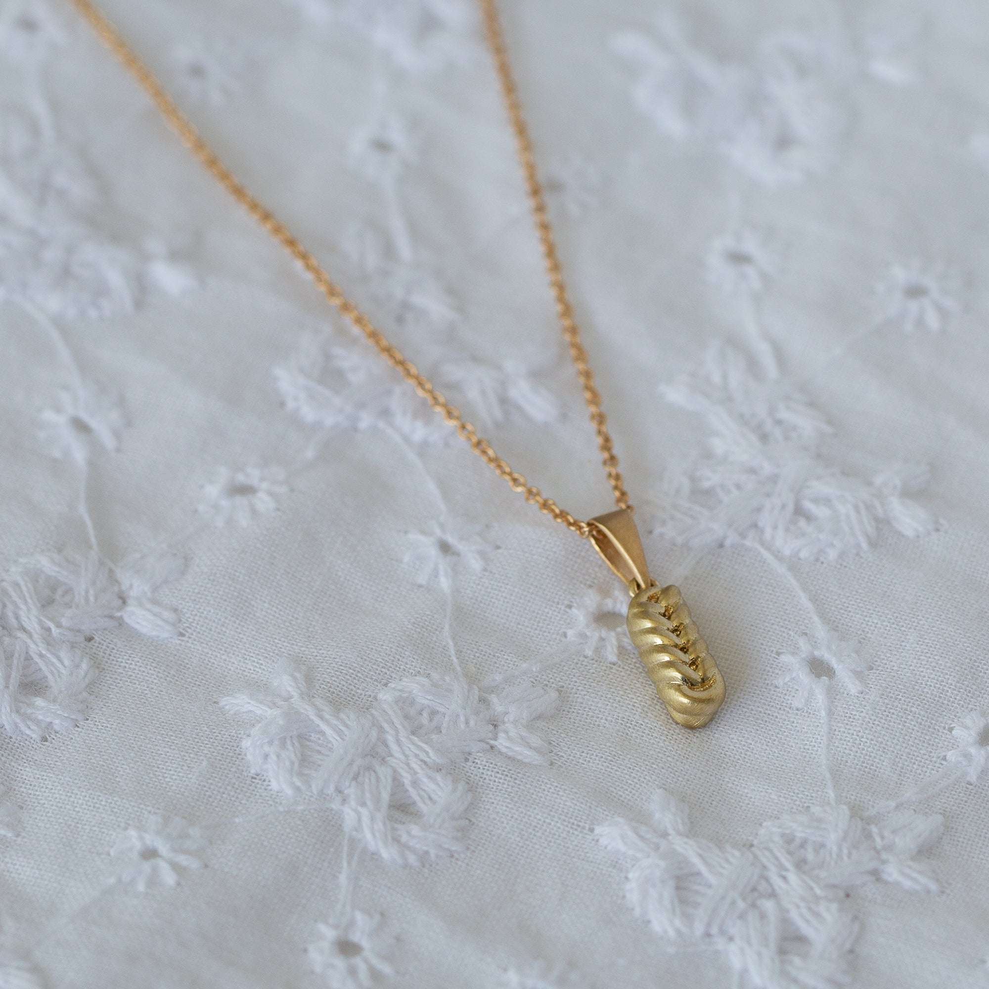 תקריב של שרשרת זהב עדינה עם תליון זהב על בד רקום לבן