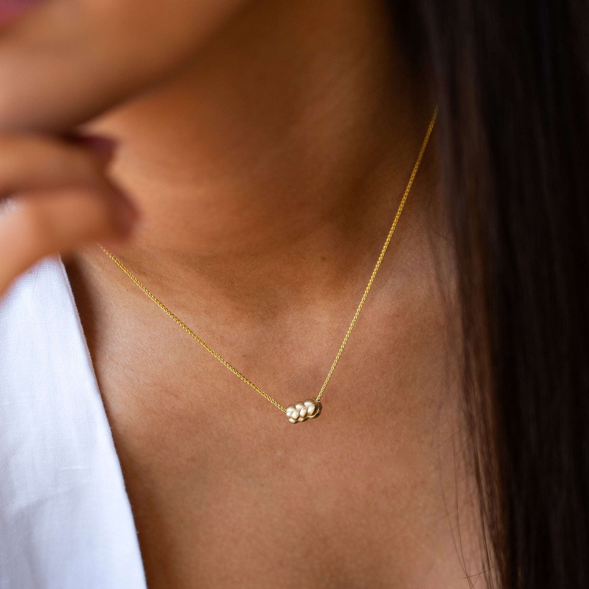 תקריב של צוואר של אישה שעונדת שרשרת זהב צהוב עם תליון קלוע