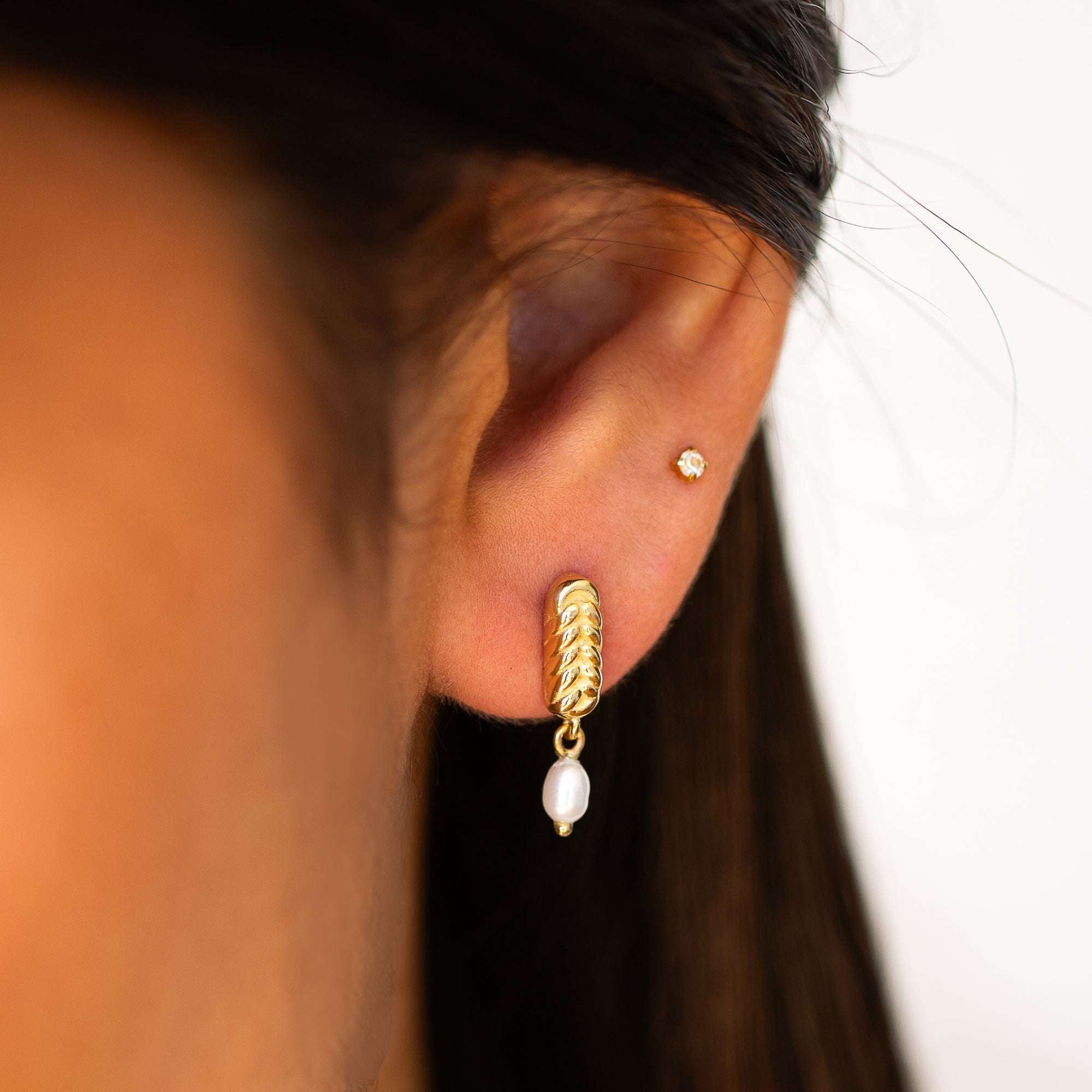 תקריב של אוזן שעונדת עגילי פנינה וזהב 14K צהוב בעיצוב קלוע