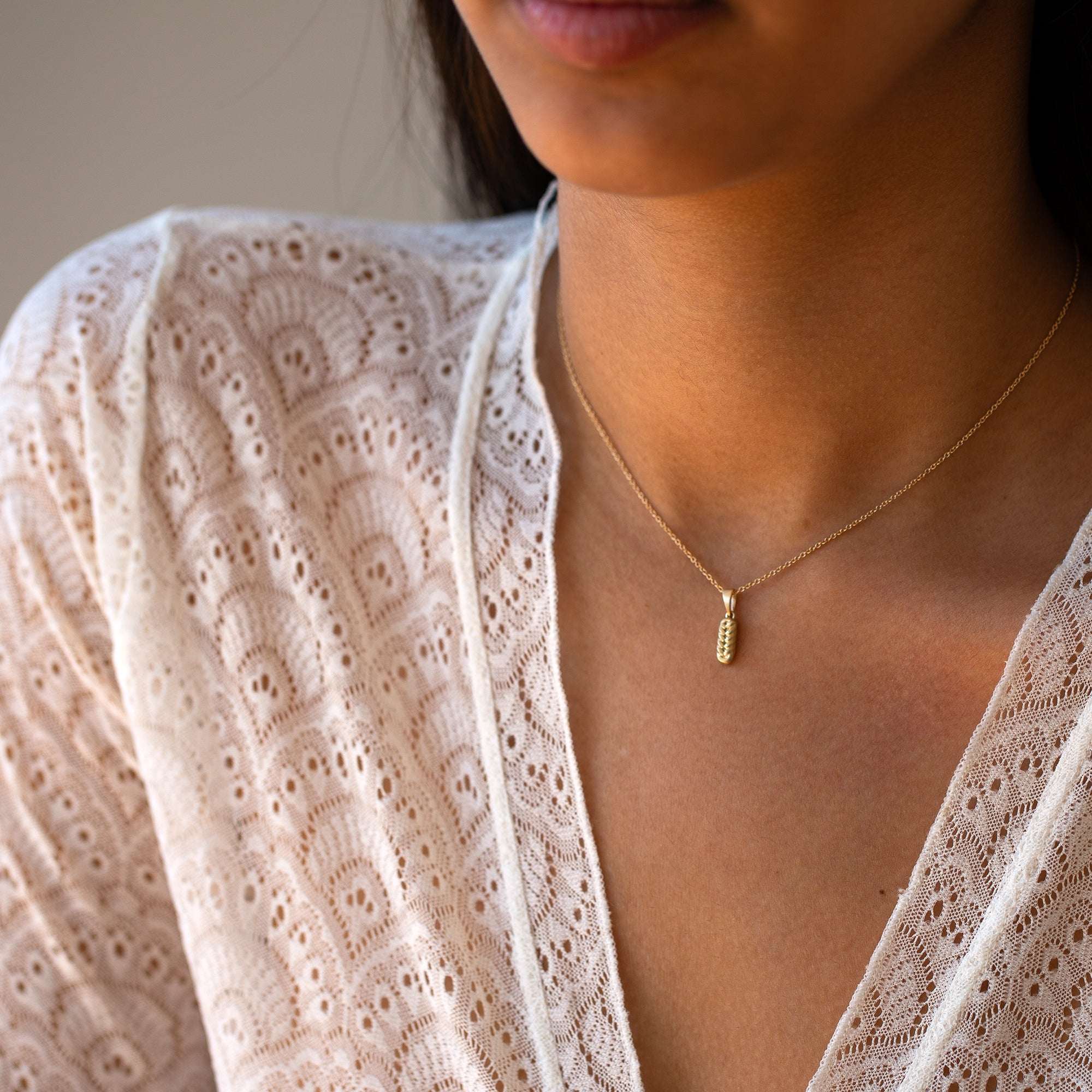 תקריב של אישה שעונדת שרשרת זהב דקה עם תליון קלוע בצורת חלב בזהב צהוב וחולצת תחרה