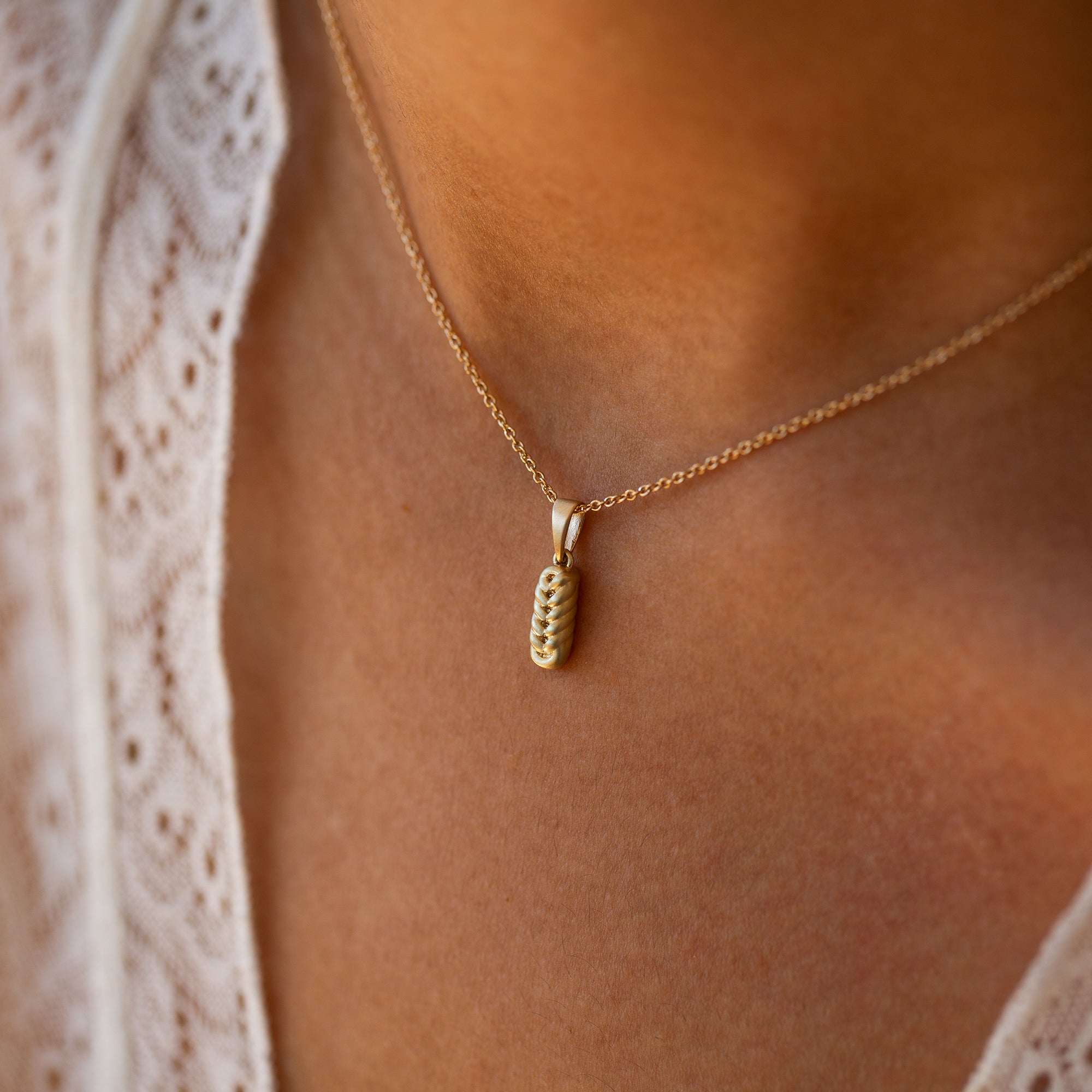 תקריב של אישה שעונדת שרשרת זהב עם תליון קלוע מזהב צהוב