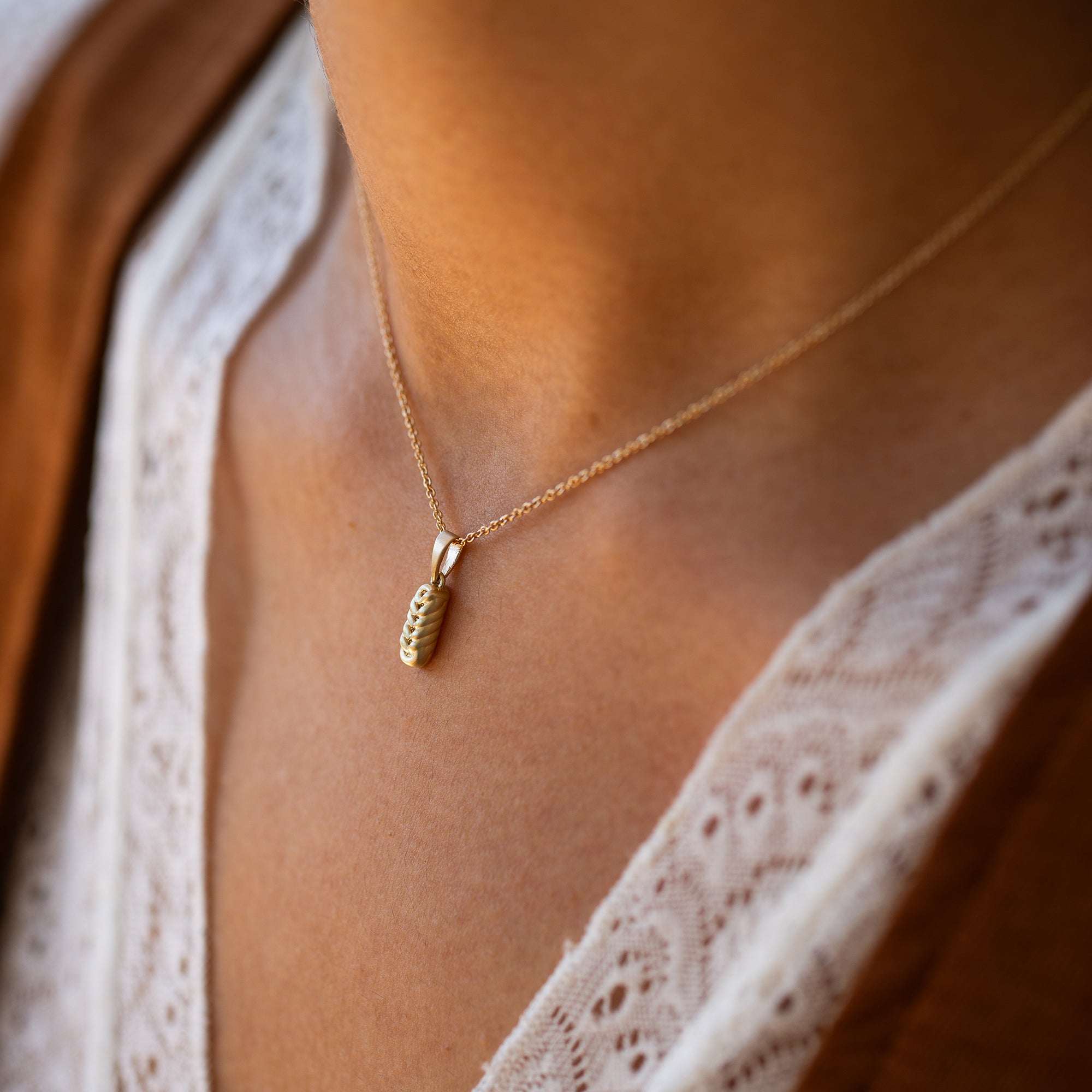 תקריב של שרשרת זהב דקה עם תליון קלוע עדין