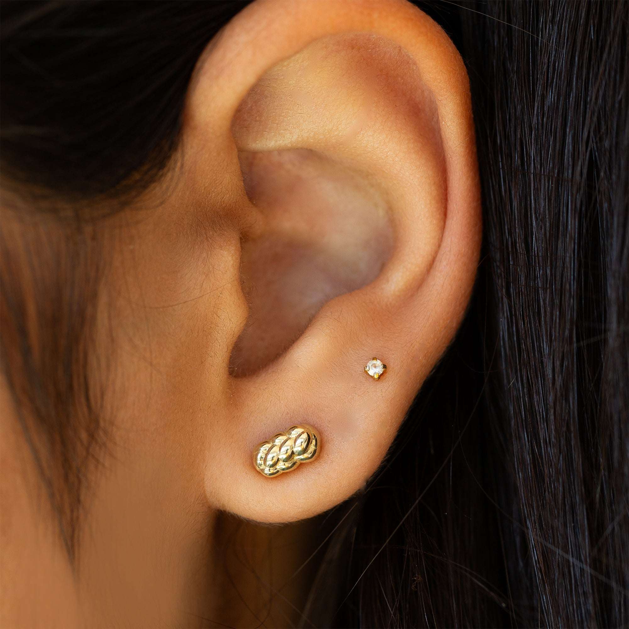 תקריב של אוזן של אישה שעונדת עגילי זהב צמודים בזהב צהוב