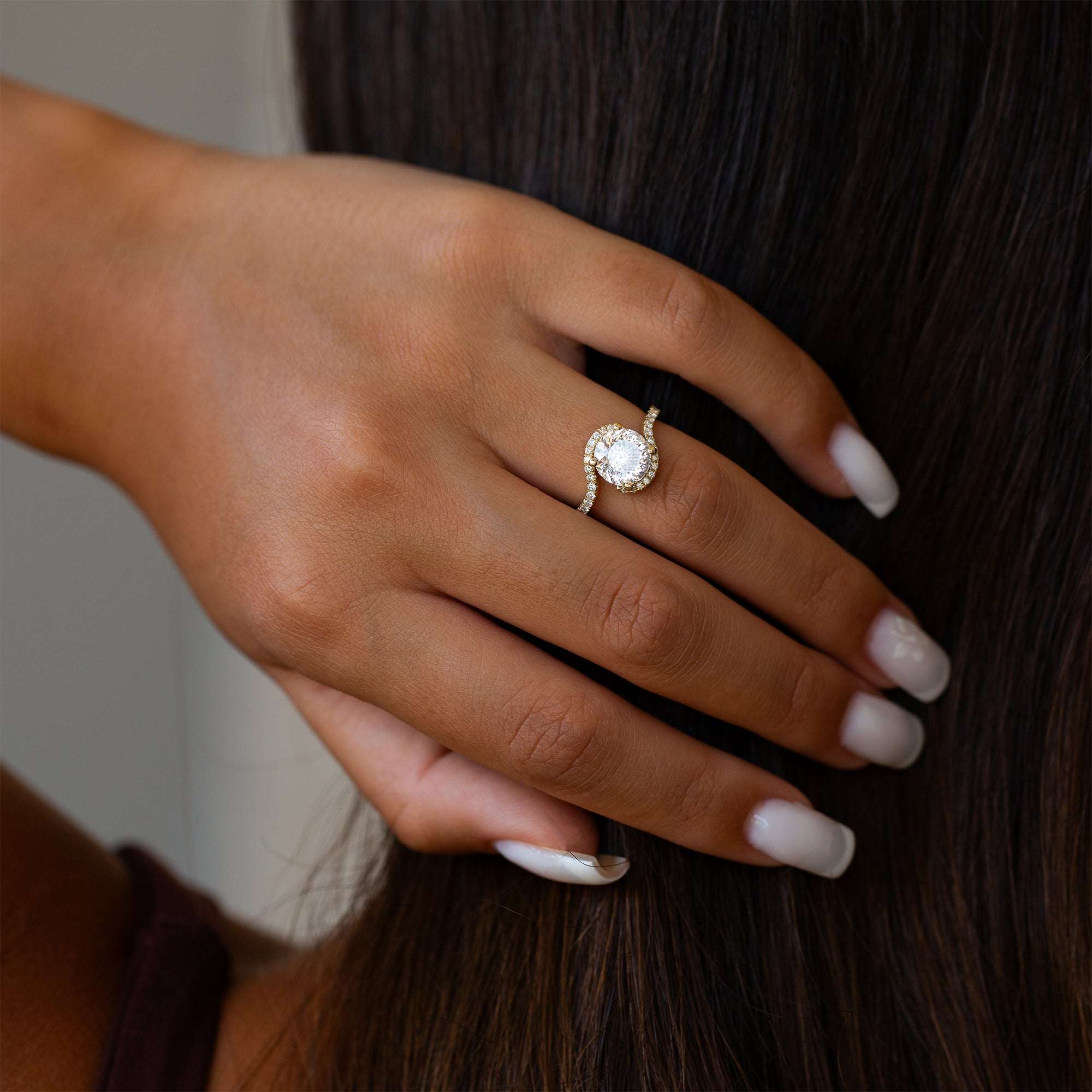 יד של אישה שעונדת טבעת מוסונייט משובצת יהלומי מעבדה, מחזיקה את ידה על שיערה