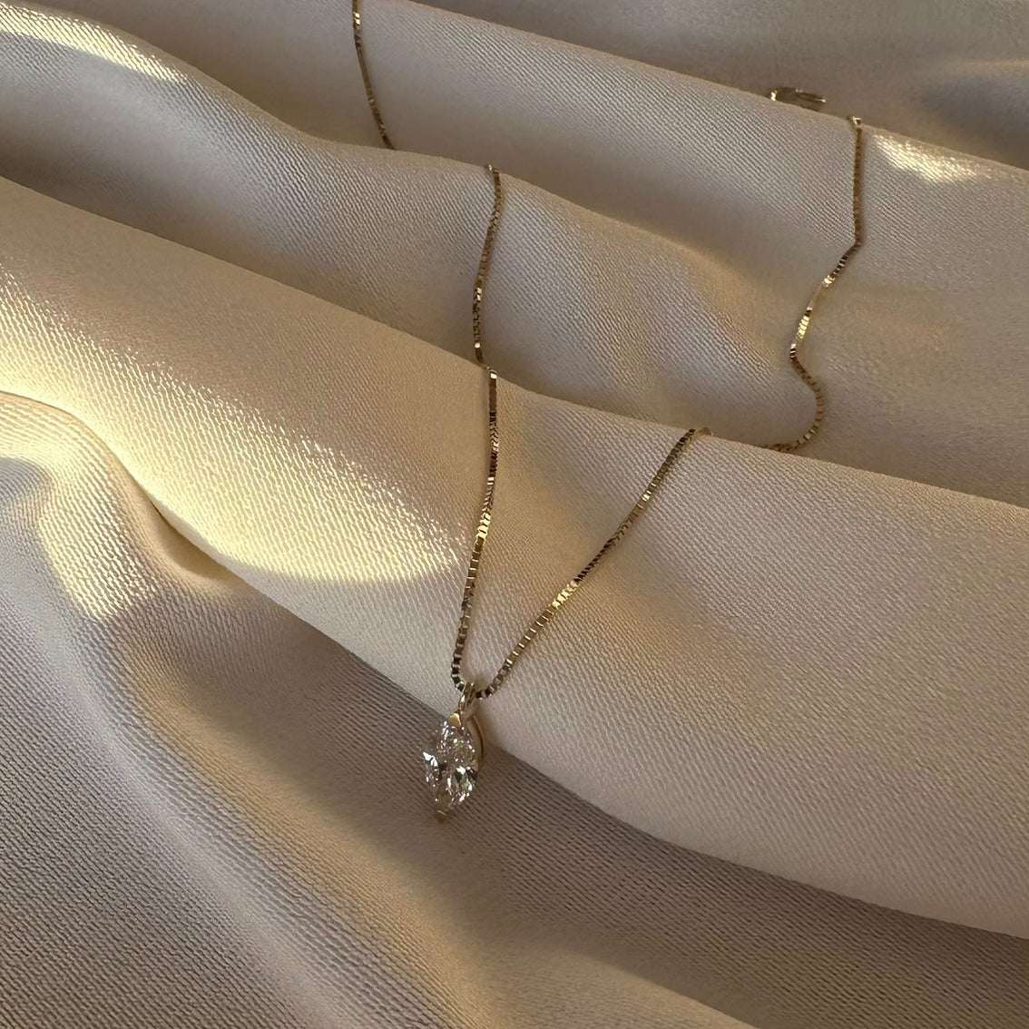 תקריב של שרשרת זהב עדינה עם תליון יהלום מעבדה 1 קראט על רקע בד לבן