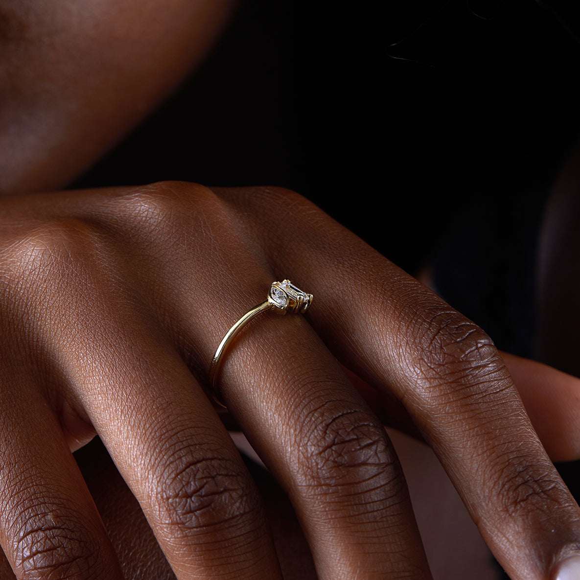 תקריב של יד של אישה שעונדת טבעת אירוסין מרובעת משובצת יהלום אמרלד קאט ומרקיזה בזהב צהוב