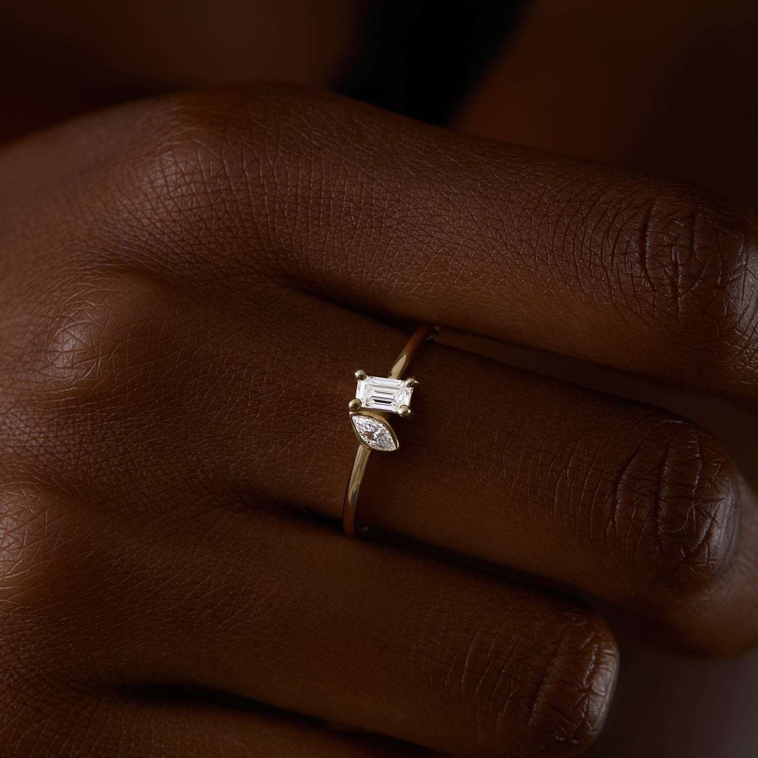 תקריב של יד של אישה שעונדת טבעת זהב צהוב 14 קראט משובצת יהלומי מעבדה בחיתוך אמרלד ומרקיזה